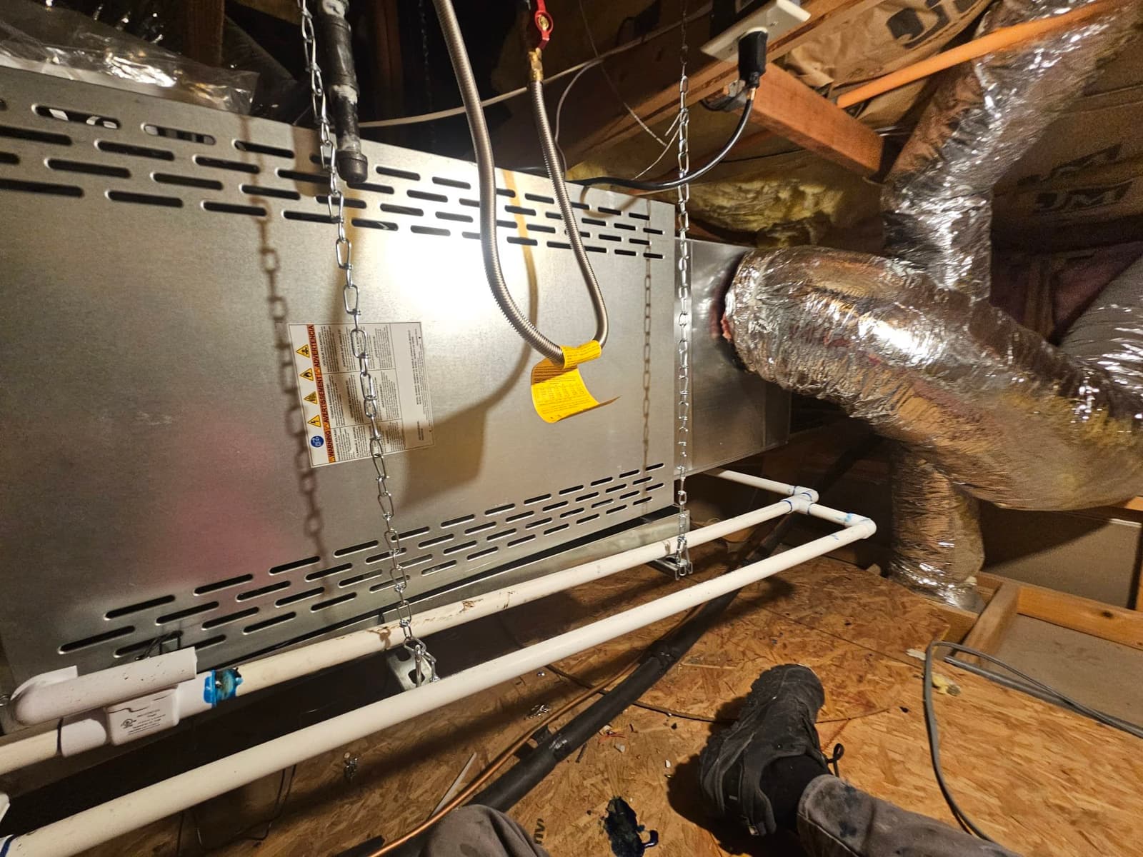 Horizontal air handler hung in the attic with insulated duct connections and dual PVC condensate drain lines installed and supported.