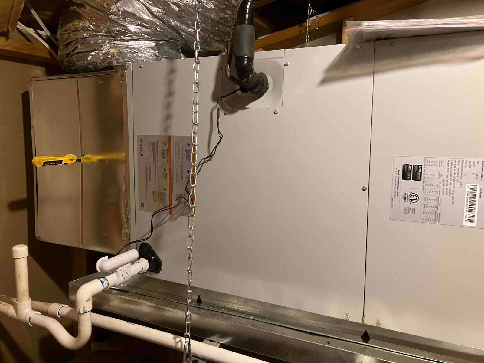Horizontal attic air handler hung on chains with insulated duct connection and PVC condensate drain assembly installed.