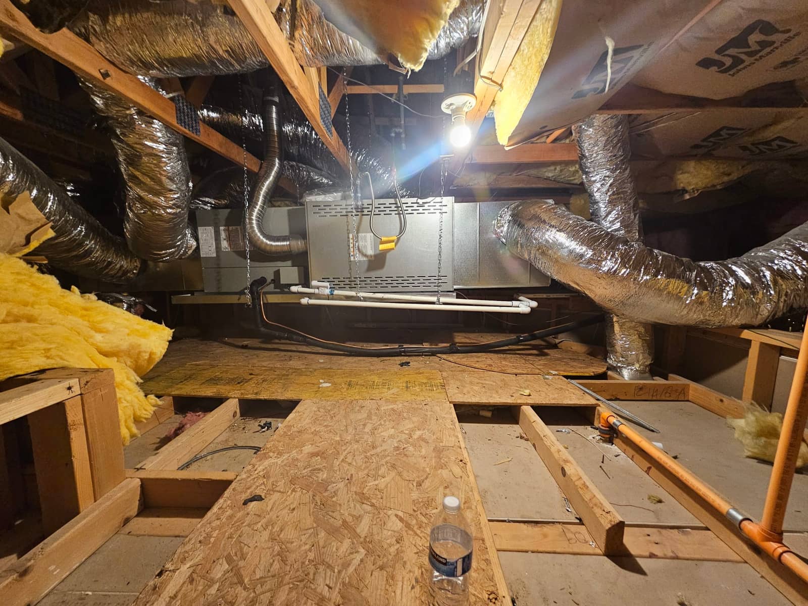 Horizontal attic air handler installed with insulated flex ducts, condensate drain piping, and secured platform under attic lighting.