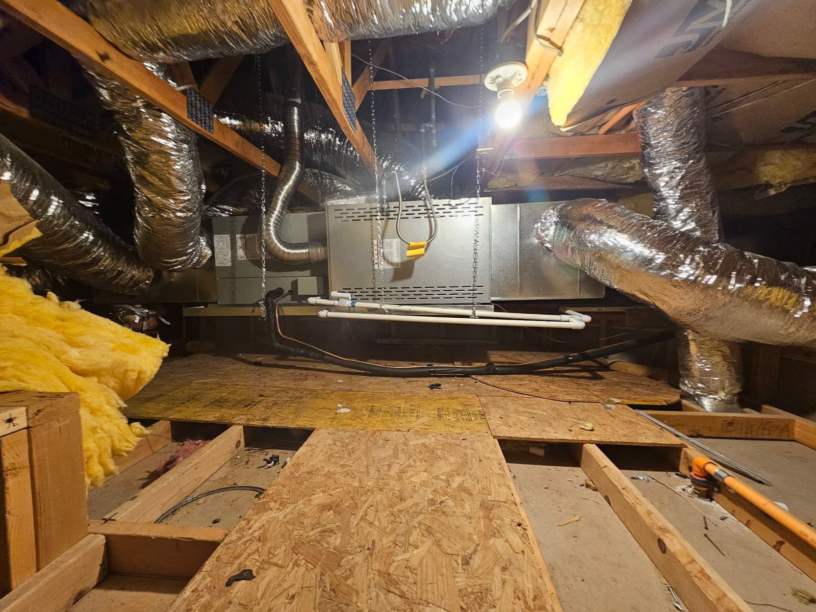 Horizontal attic air handler installed with insulated flex ducts, condensate drain piping, and suspension chains visible in the attic space.