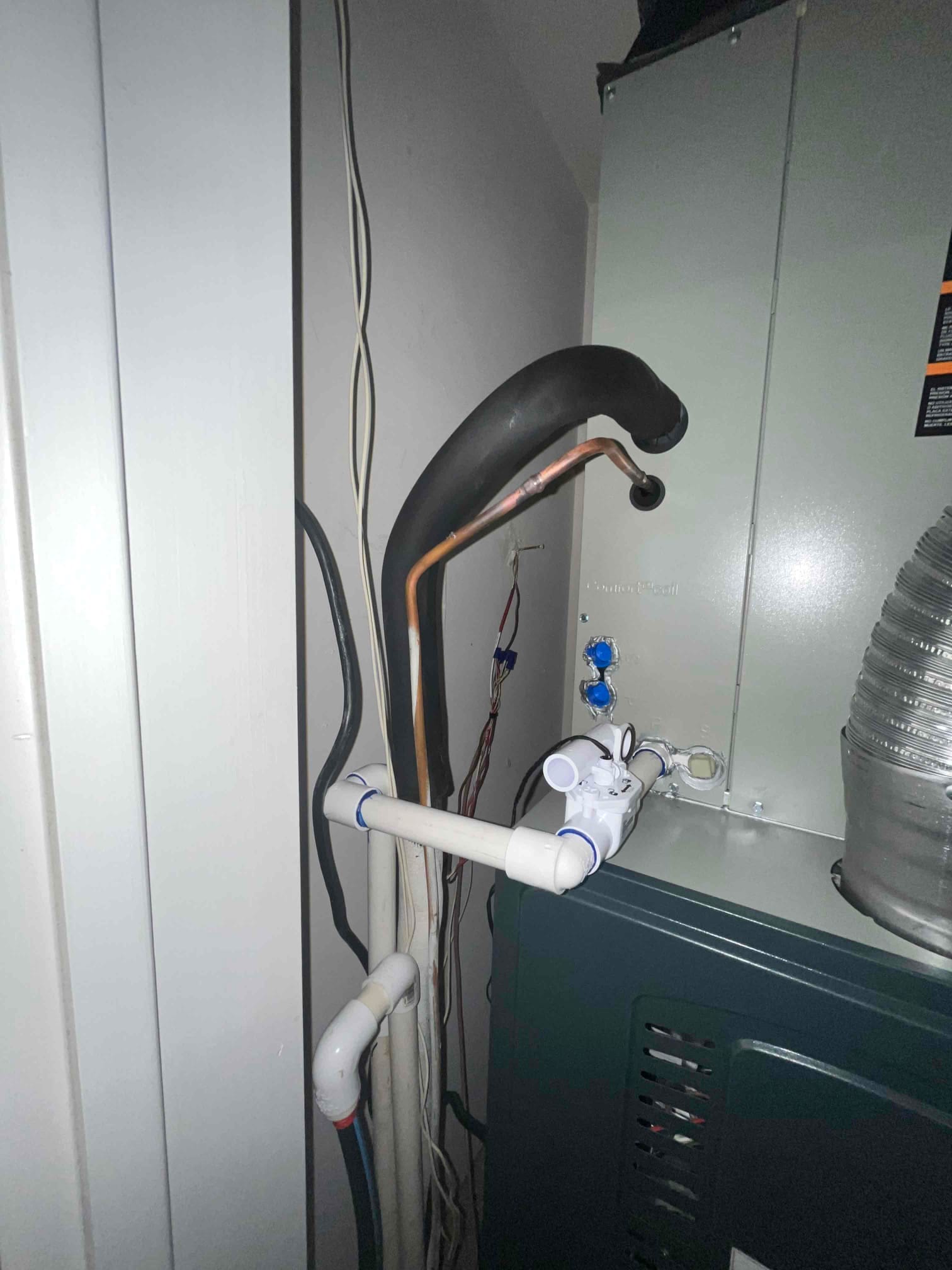 Indoor furnace and coil cabinet with connected condensate drain assembly, insulated suction line, liquid line, and wiring routed along the side.