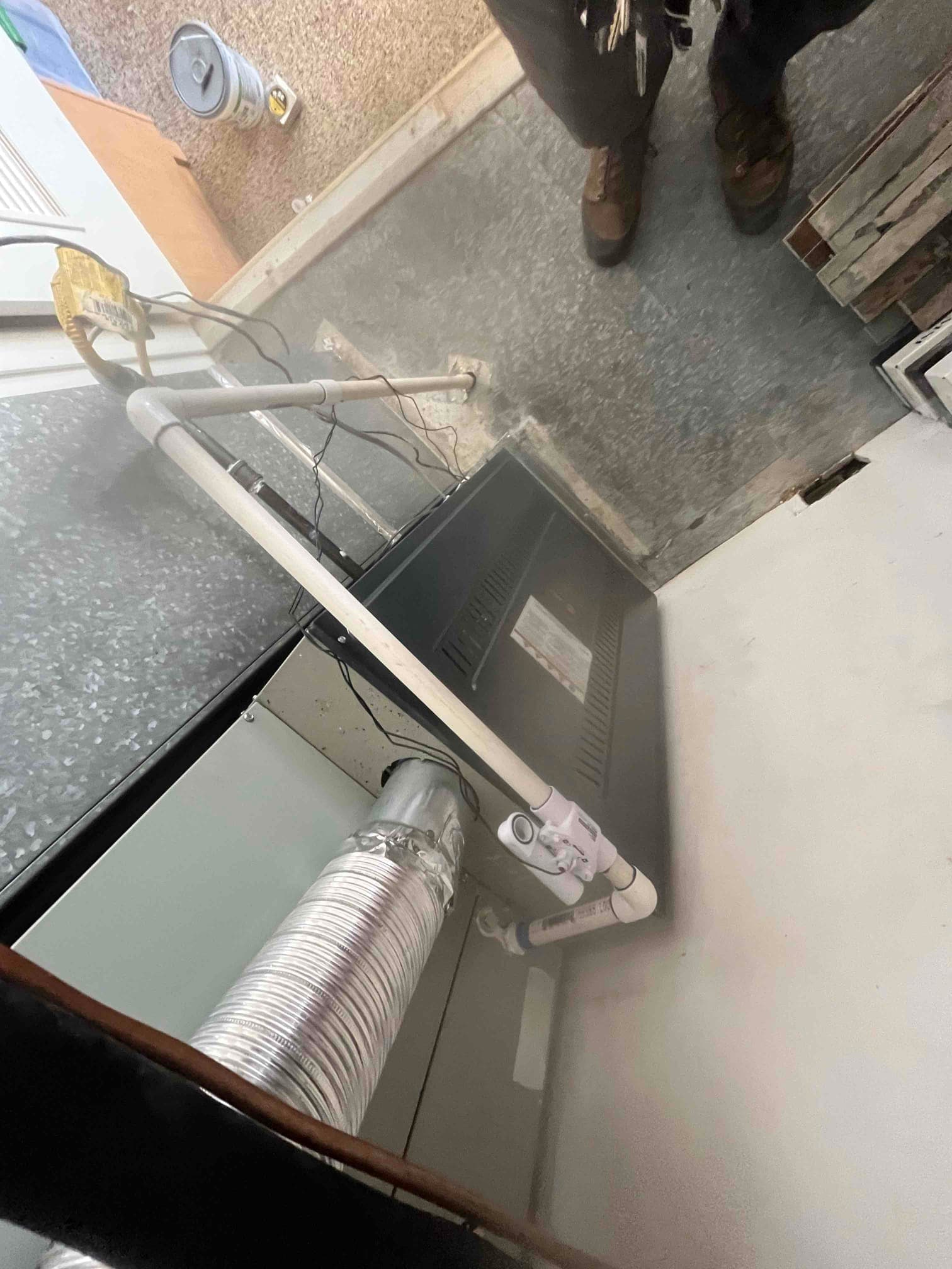 Indoor furnace and coil cabinet set in place with PVC condensate drain and flexible duct connection visible at the base.