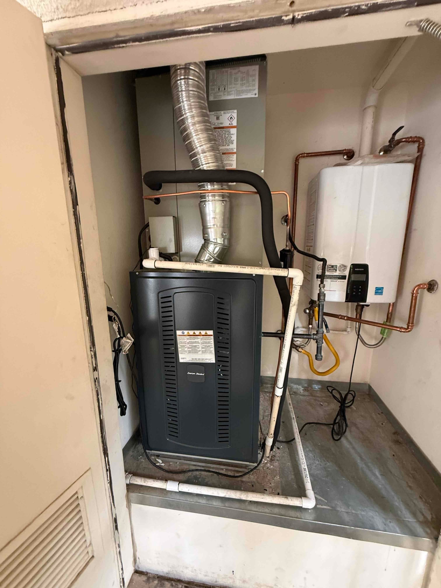 Indoor HVAC equipment set on a drain pan with insulated refrigerant lines, condensate piping, and venting connected inside the closet.