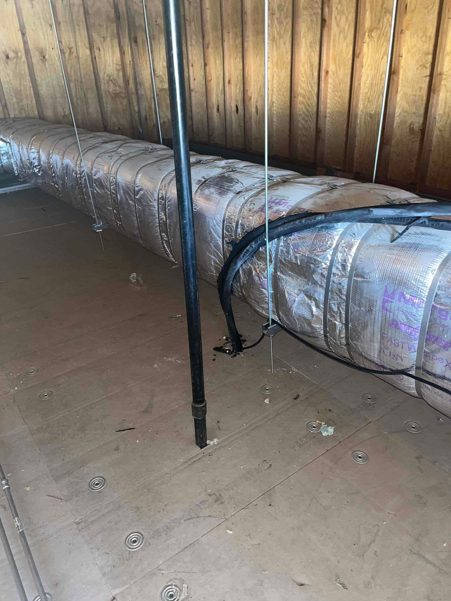 Insulated duct trunk secured in attic with hanging straps and supported over a clean work platform, with refrigerant lines routed alongside.