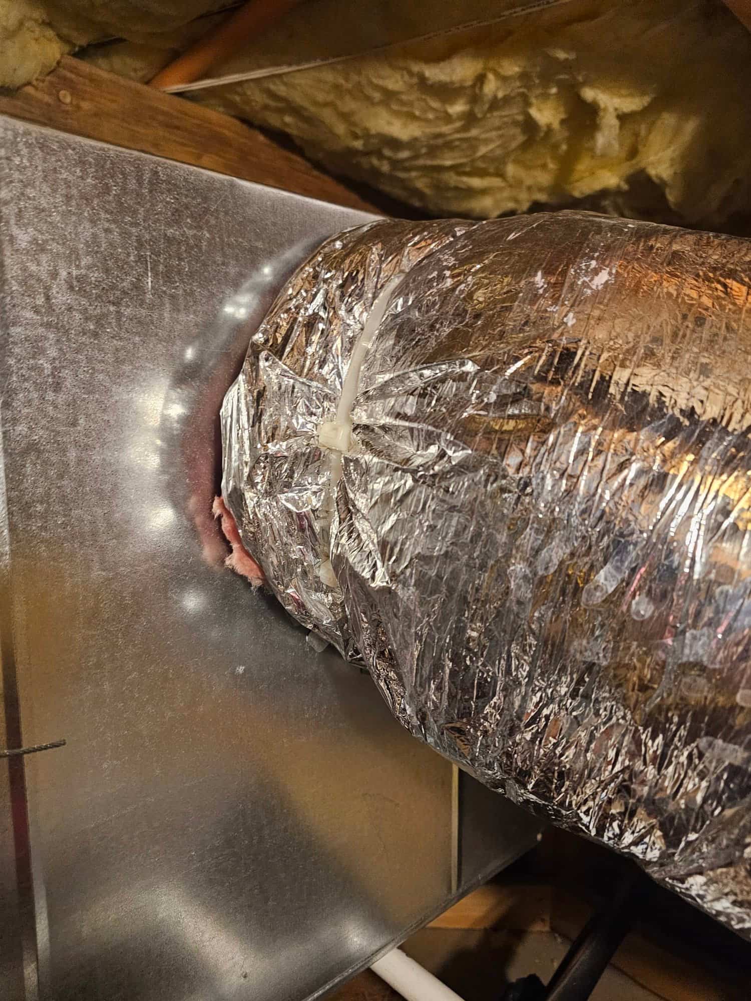 Insulated flexible duct connected to a metal plenum in the attic, secured with a zip tie and surrounded by spray foam insulation.
