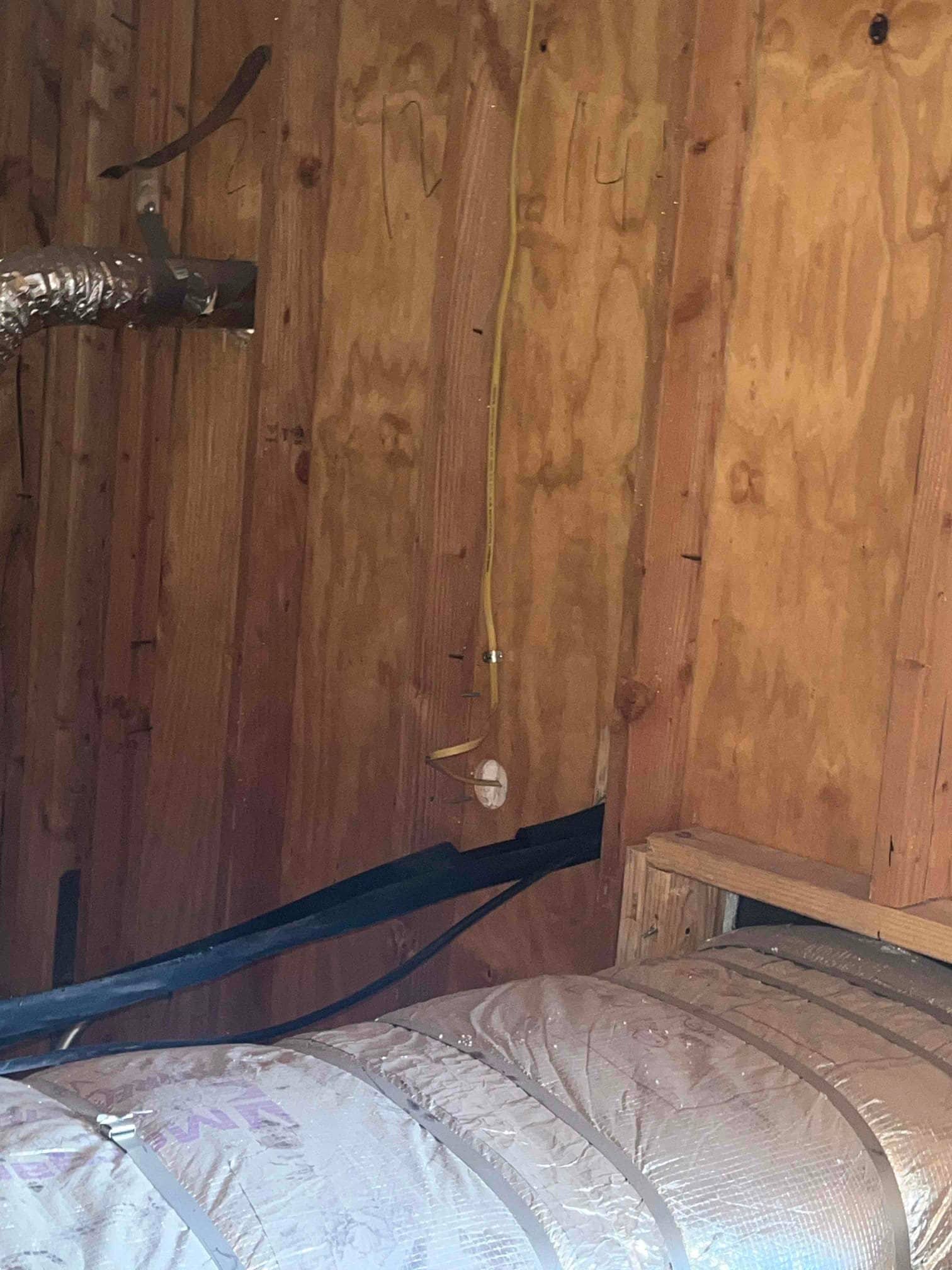 Insulated flexible duct and refrigerant line set routed through a plywood wall penetration inside the mechanical space.