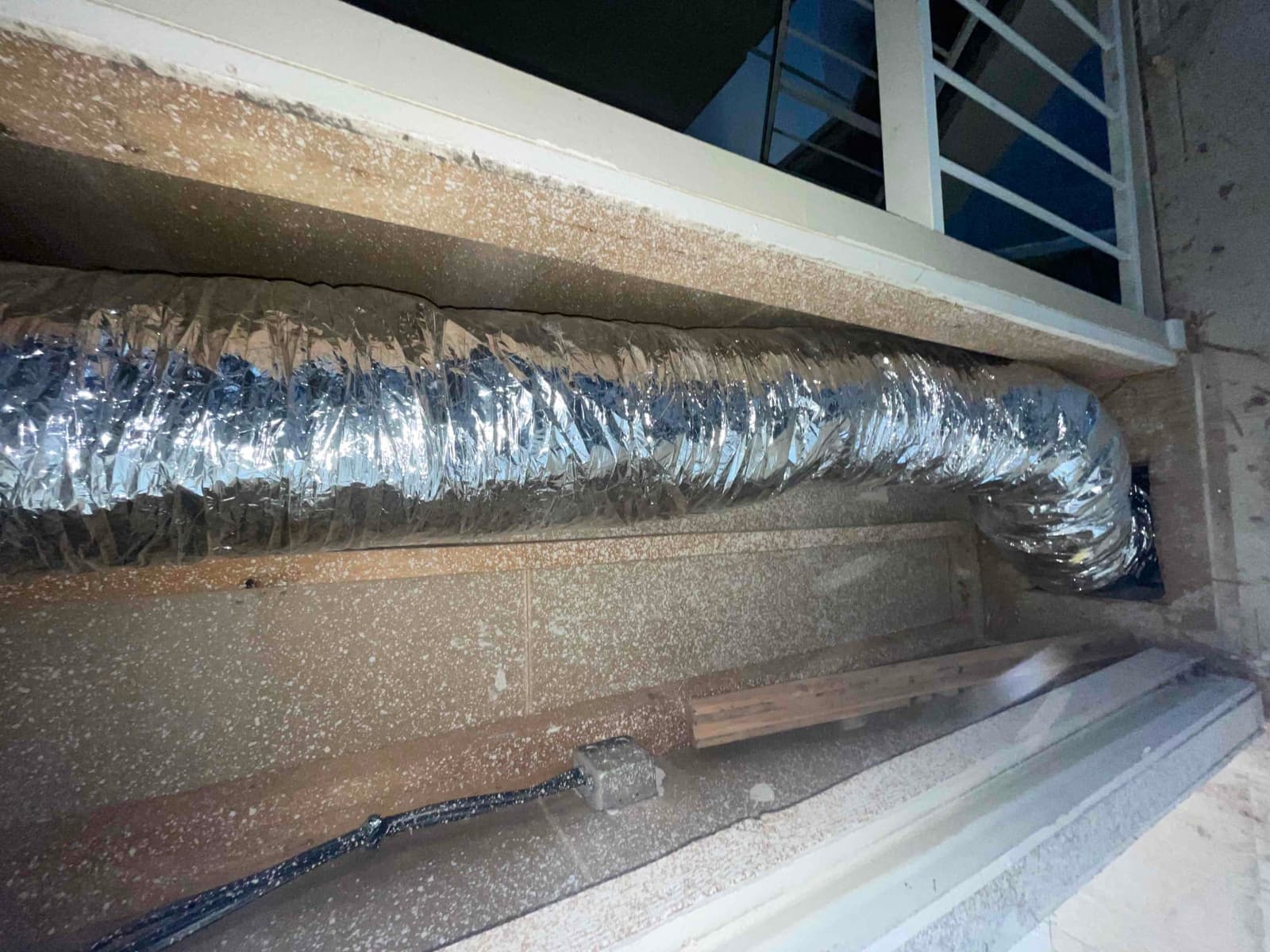 Insulated flexible duct run installed in a framed soffit, with a tight elbow connection sealed at the wall penetration.