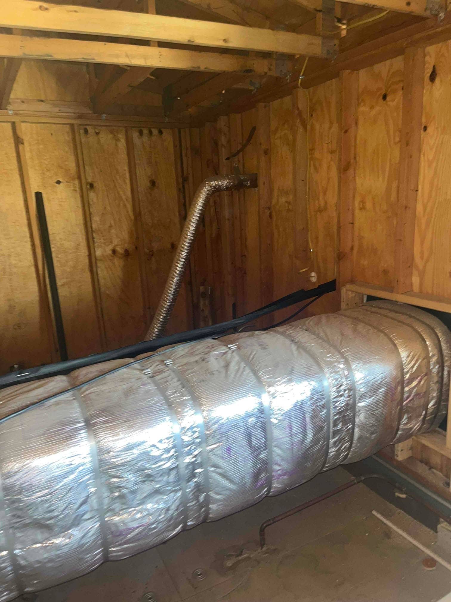 Insulated flexible ductwork routed through a framed utility space, with refrigerant and drain lines organized along the floor and wall.