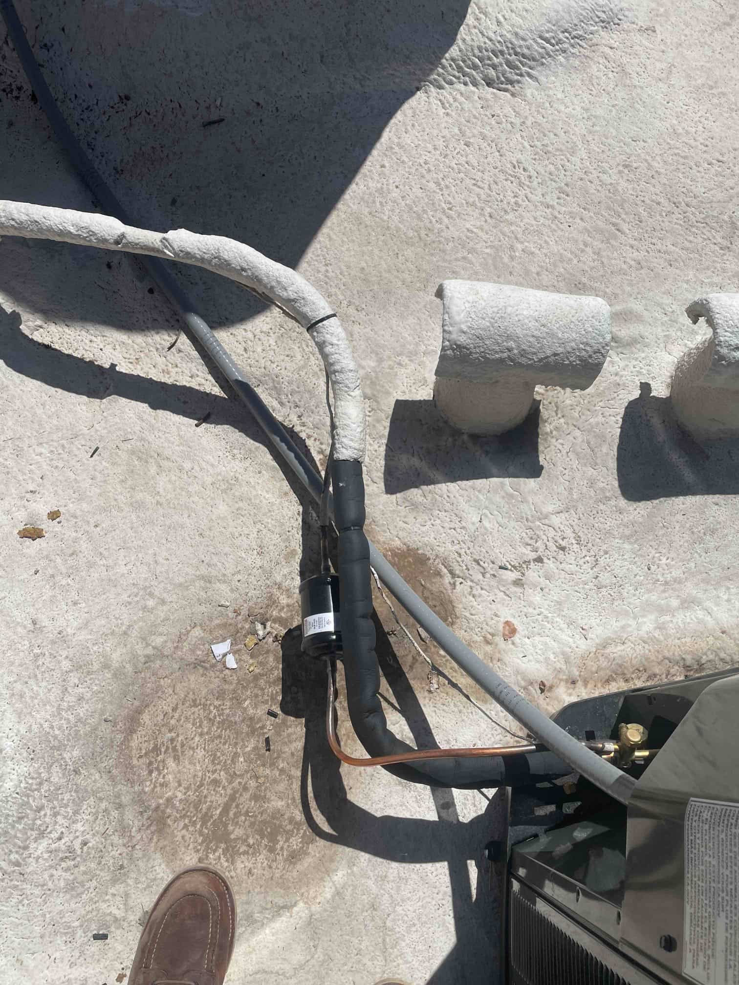 Insulated refrigerant line set and filter-drier connected at the outdoor condenser, with control cable and service valves visible.