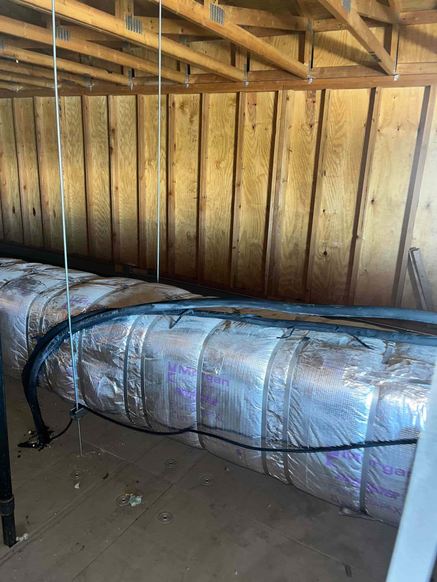 Insulated supply trunk duct secured in an attic space with support hangers and refrigerant line set routed alongside.