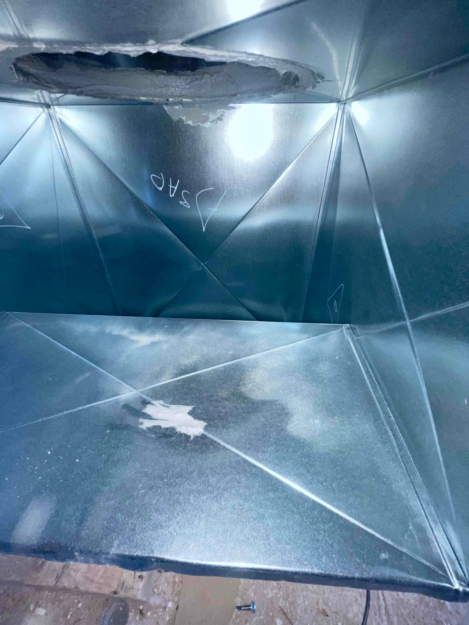 Interior of new sheet-metal duct plenum showing sealed seams and an opening cut for a takeoff connection.