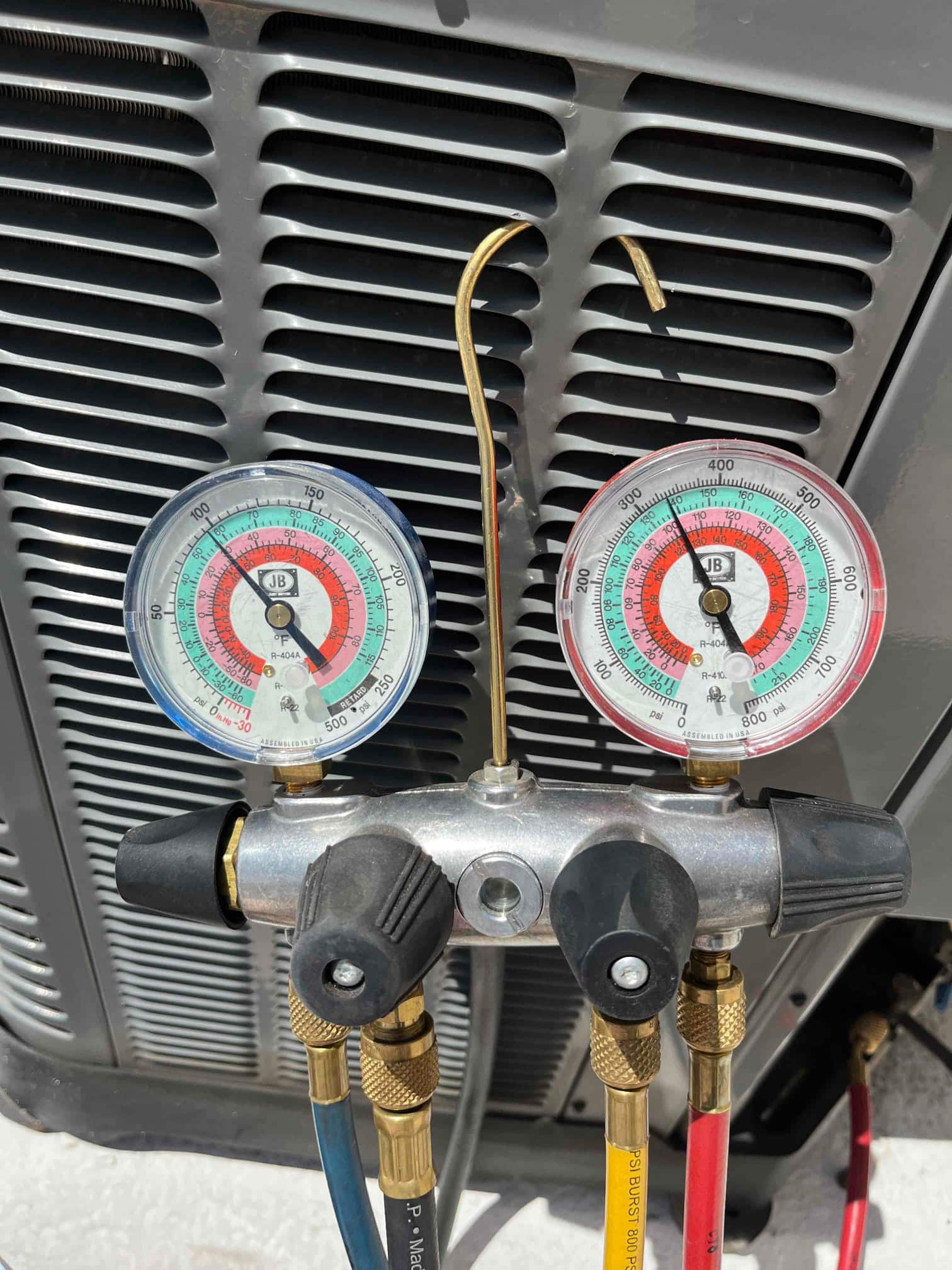 Manifold gauge set connected to the outdoor condenser service ports during R-410A charging, showing high- and low-side pressures on analog dials.