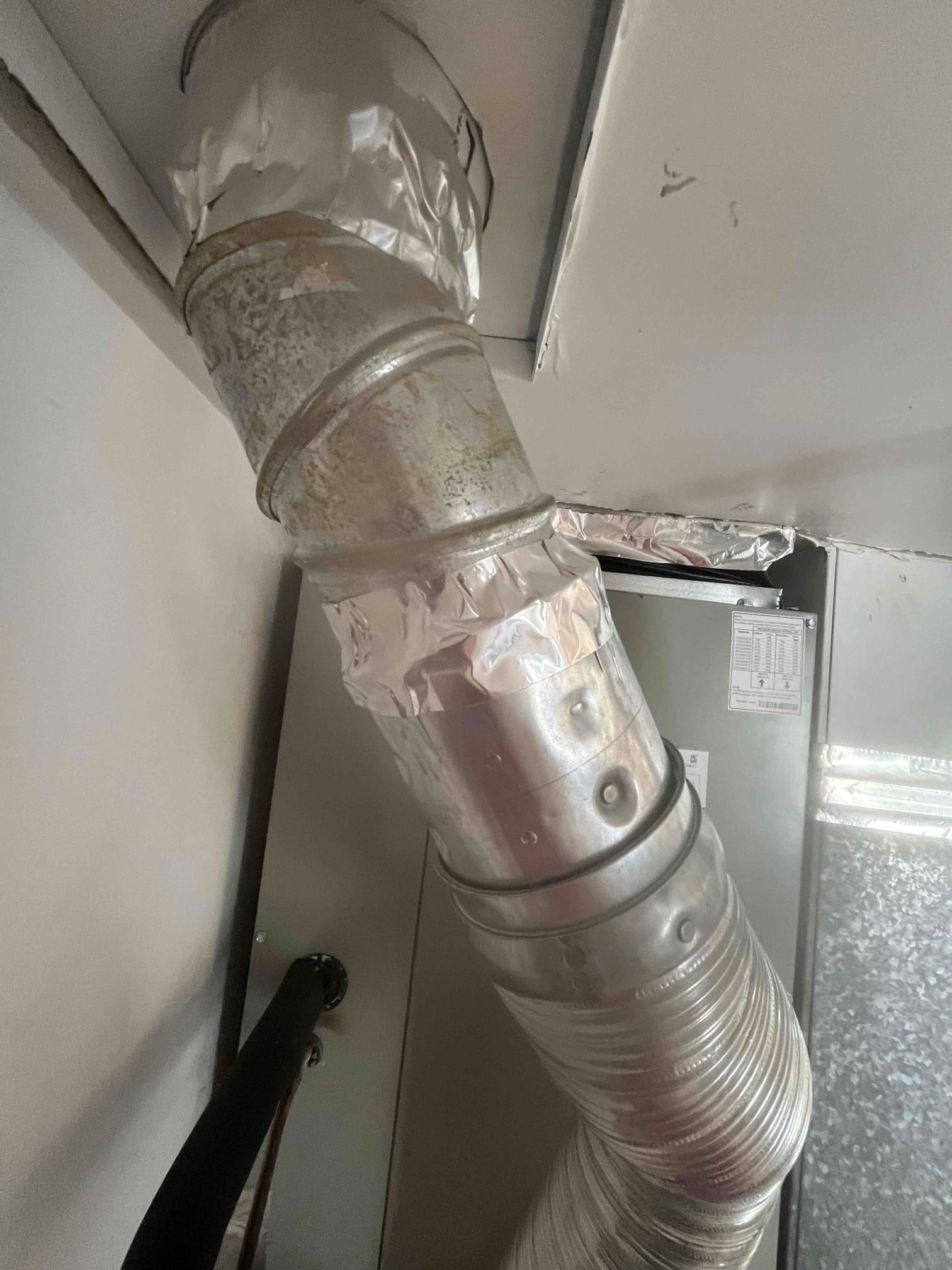 Metal duct transition sealed with foil tape connects to the furnace cabinet, showing completed airflow ductwork at the indoor unit.