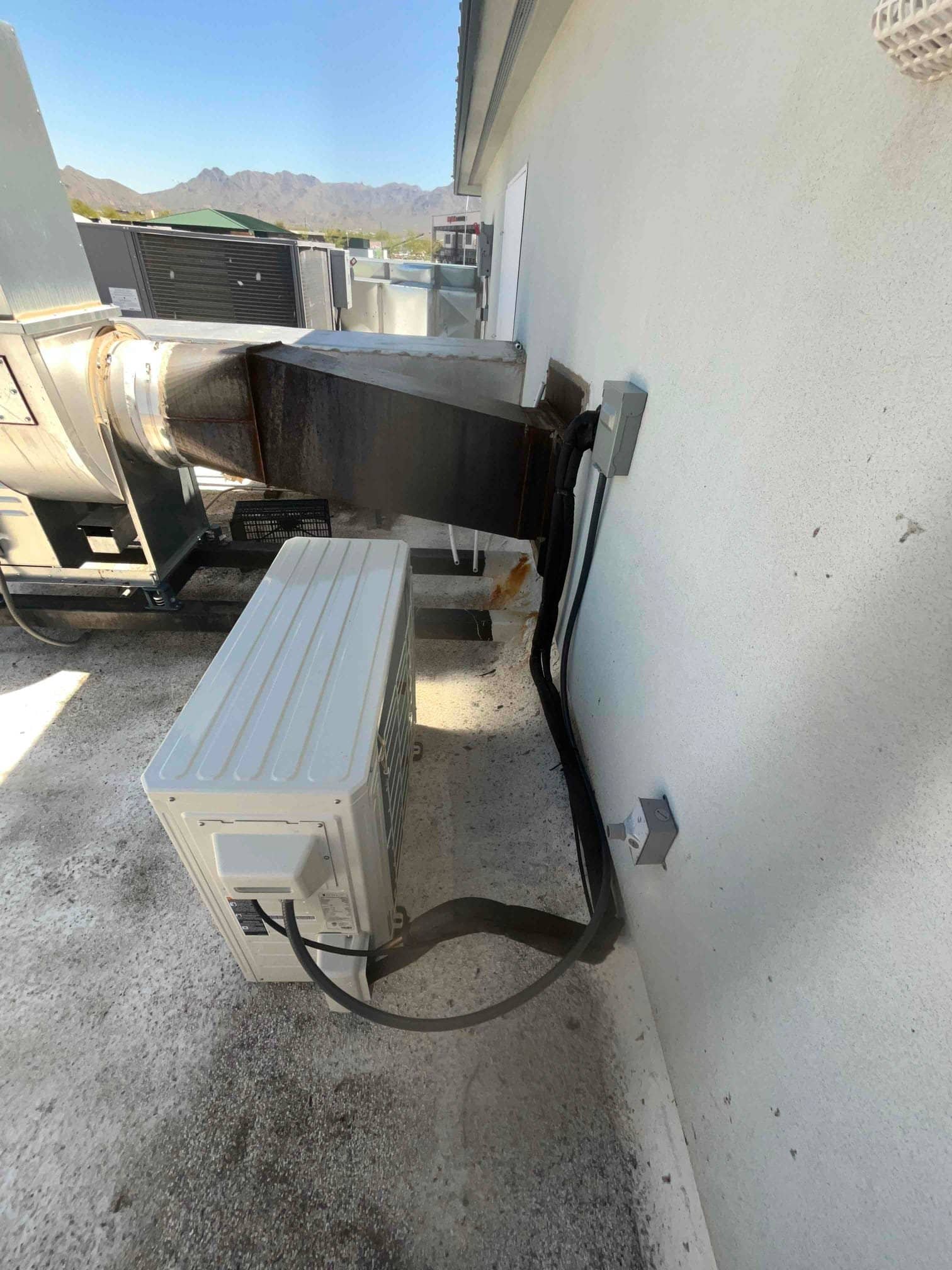 Mini‑split outdoor unit set on the rooftop with insulated line set and electrical whip routed to wall-mounted disconnect.