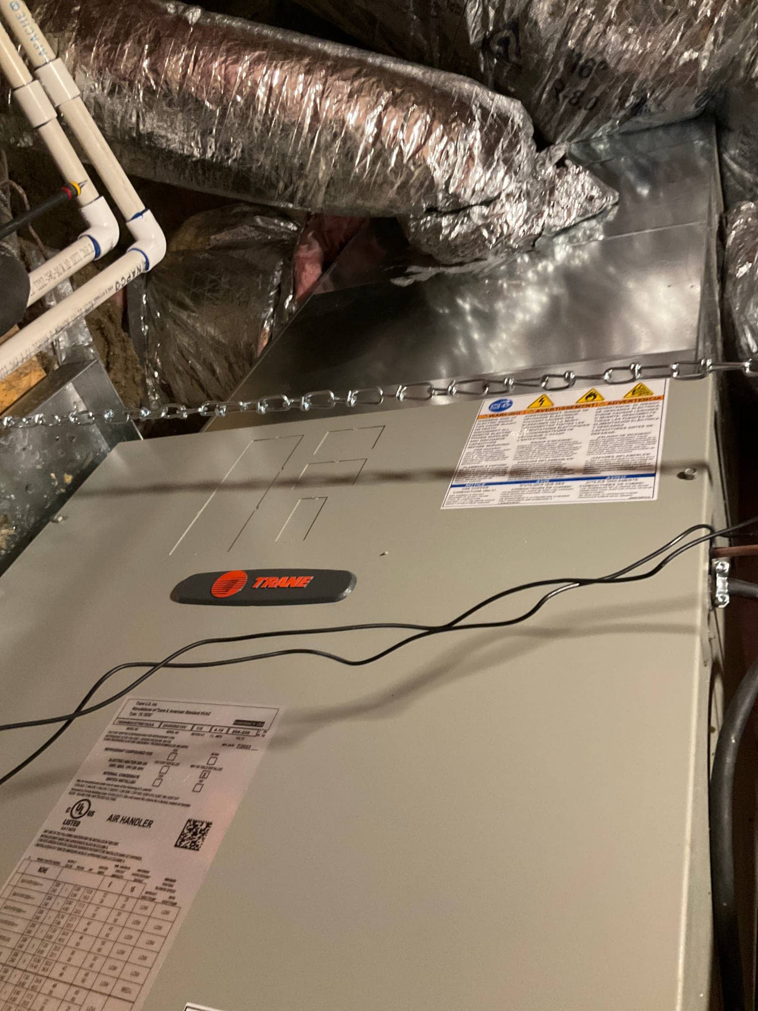 New air handler installed in attic with connected insulated ductwork, metal plenum transition, and supported drain piping visible.