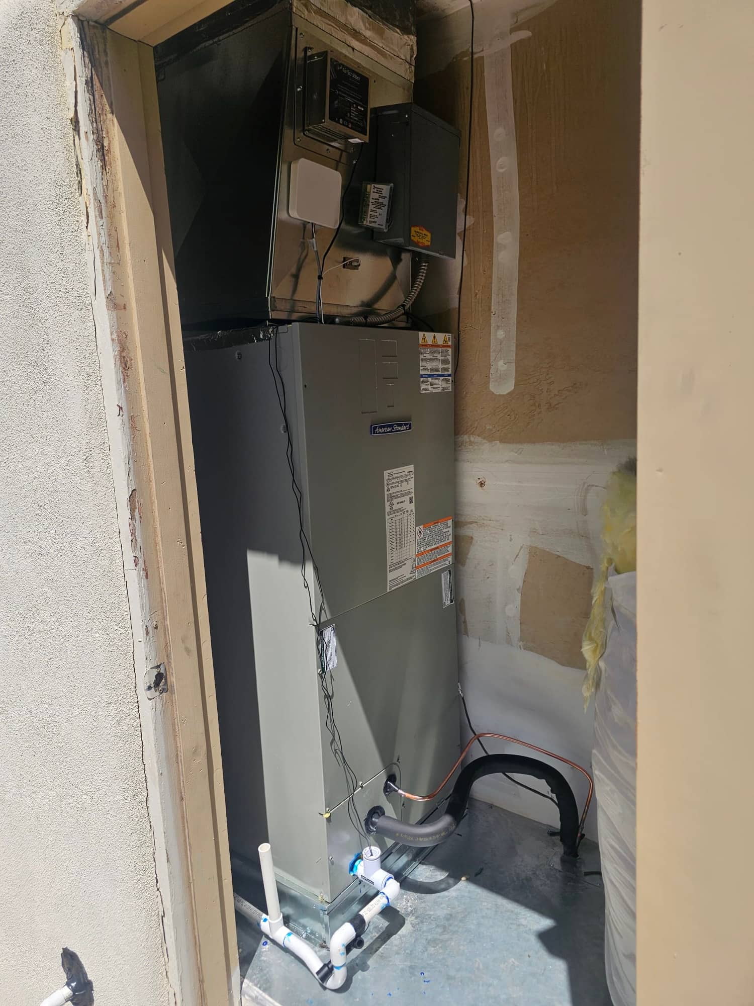 New air handler installed in a closet with insulated refrigerant lines, condensate drain piping, and electrical disconnect mounted nearby.