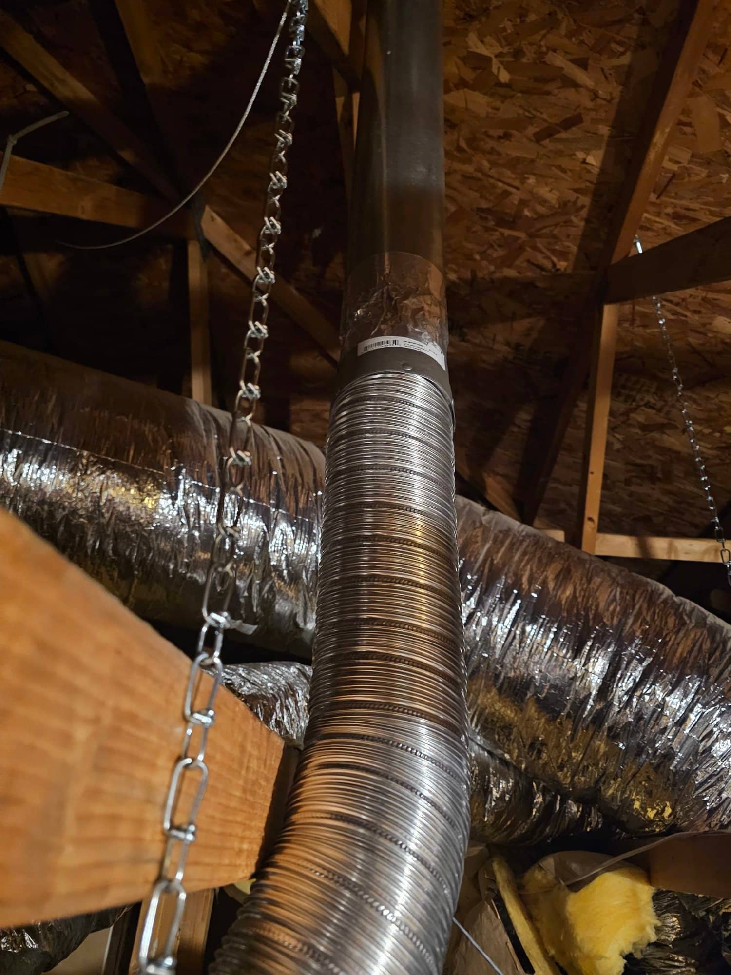 New attic ductwork with flexible insulated runs and a secured metal flue or vent pipe supported by hangers and straps.