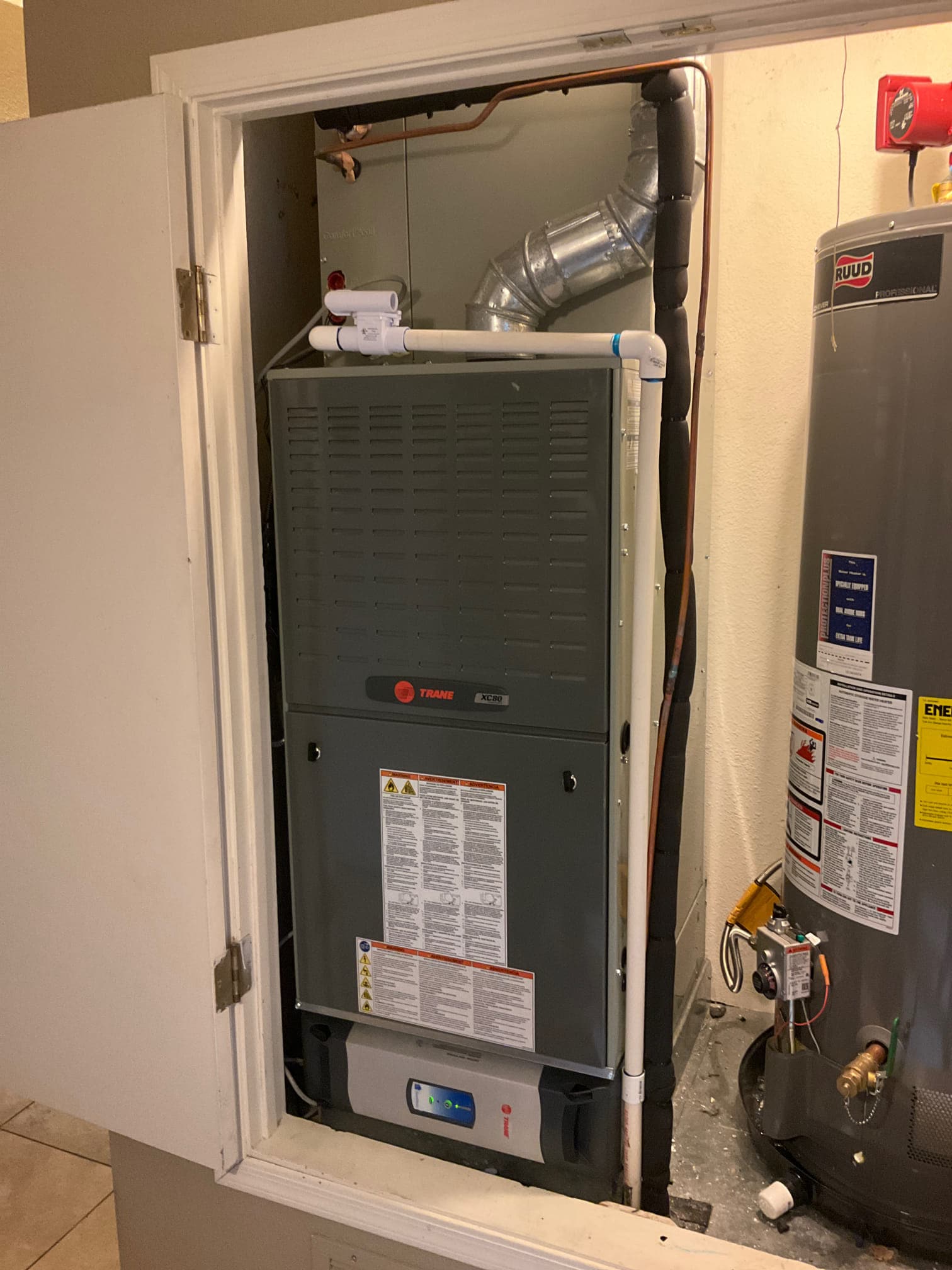 New furnace and coil installed in a closet with insulated refrigerant lines, PVC condensate drain, and adjacent water heater.