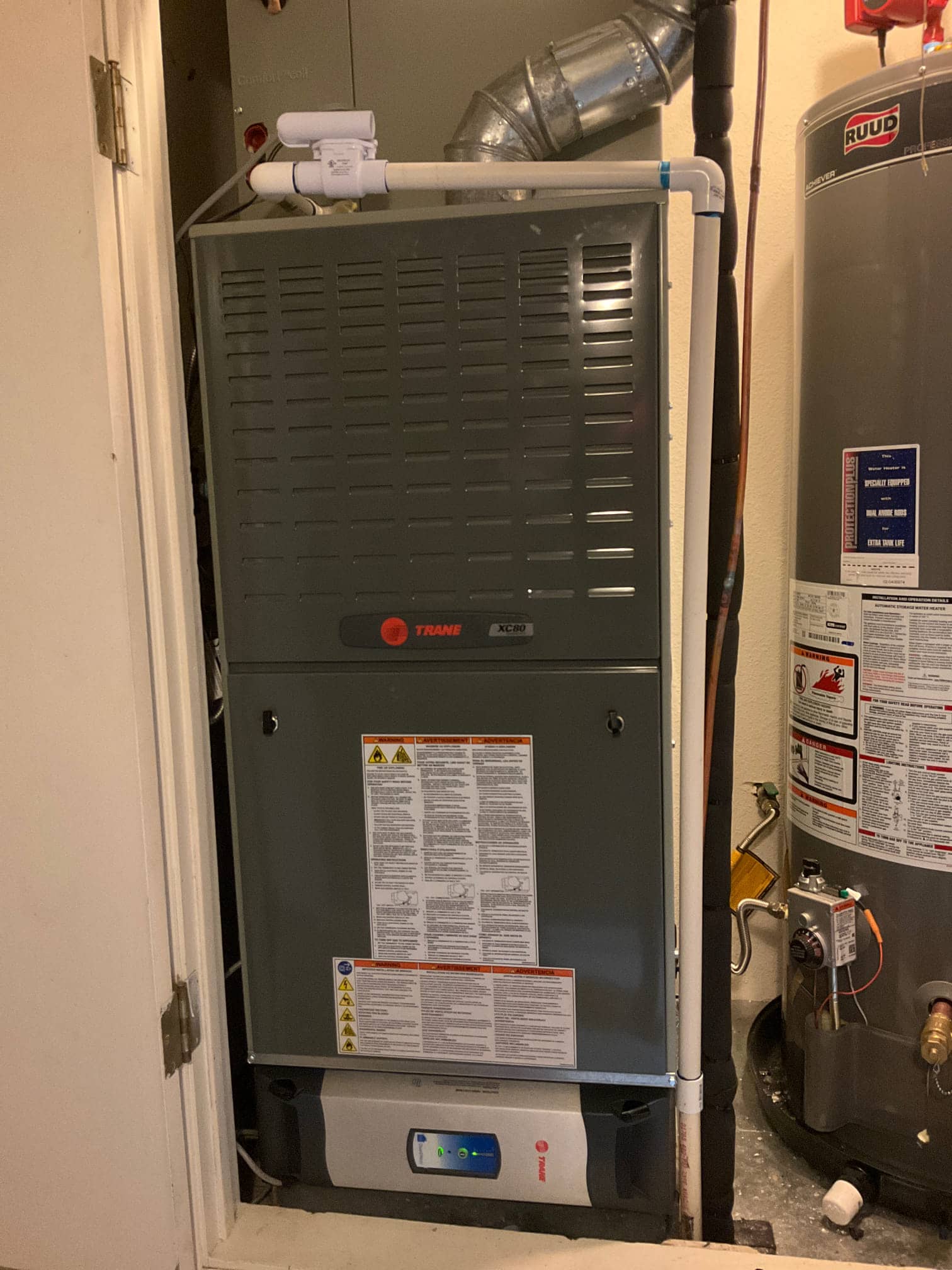 New furnace and evaporator cabinet installed in a closet with PVC condensate drain, insulated refrigerant lines, and adjacent water heater.