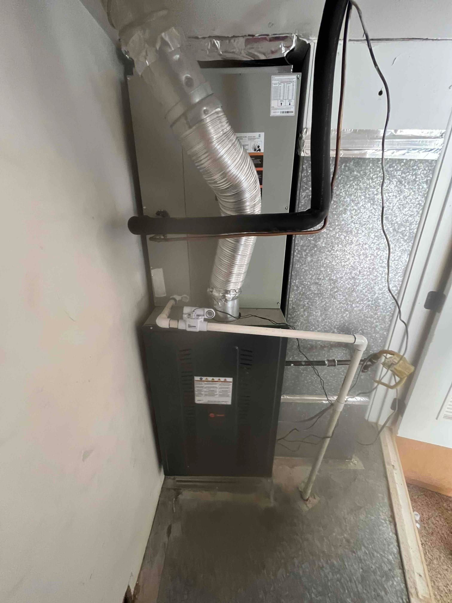 New furnace and evaporator coil installed with insulated refrigerant lines, flue venting, and condensate drain piping in the mechanical closet.