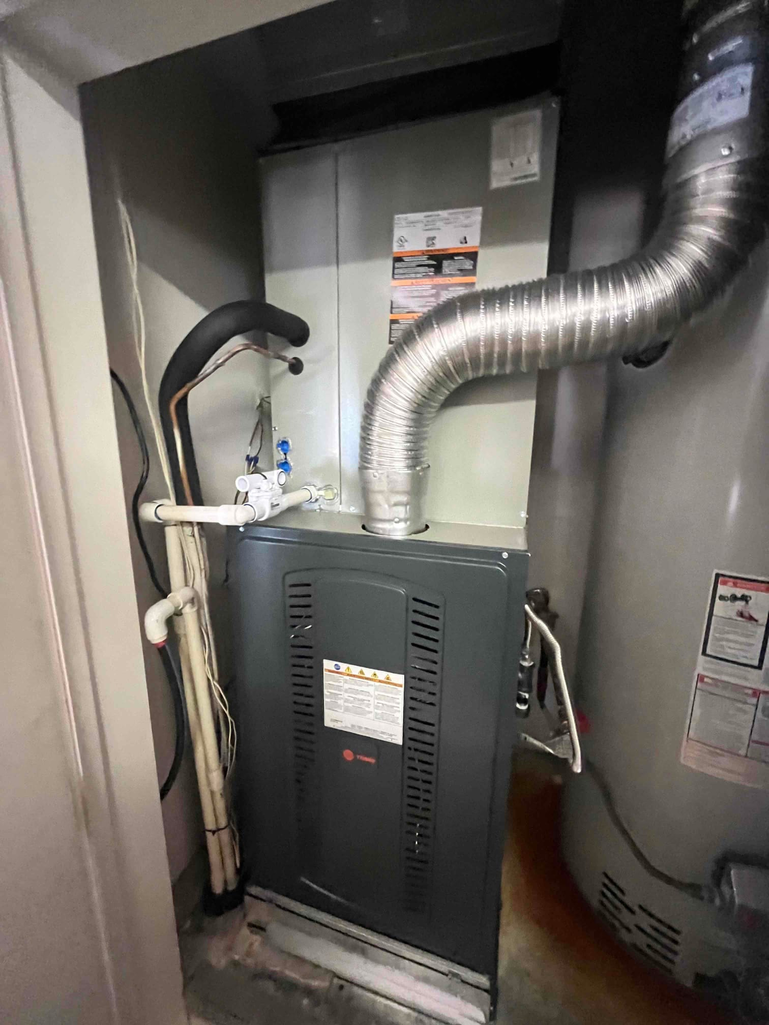 New gas furnace and evaporator coil installed in a closet, with vent connector, condensate drain, and insulated refrigerant lines routed.