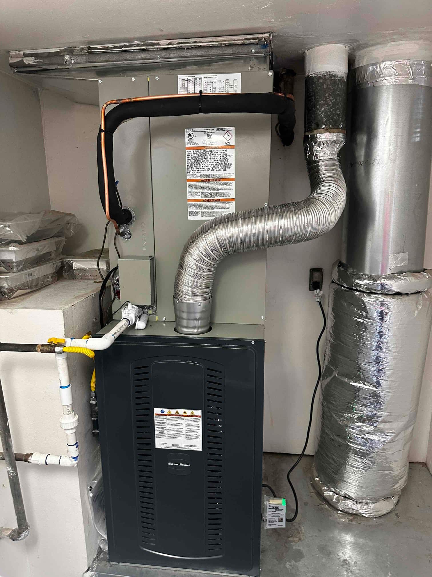 New gas furnace and evaporator coil installed with insulated refrigerant lines, venting, condensate drain, and connected ductwork in the mechanical space.