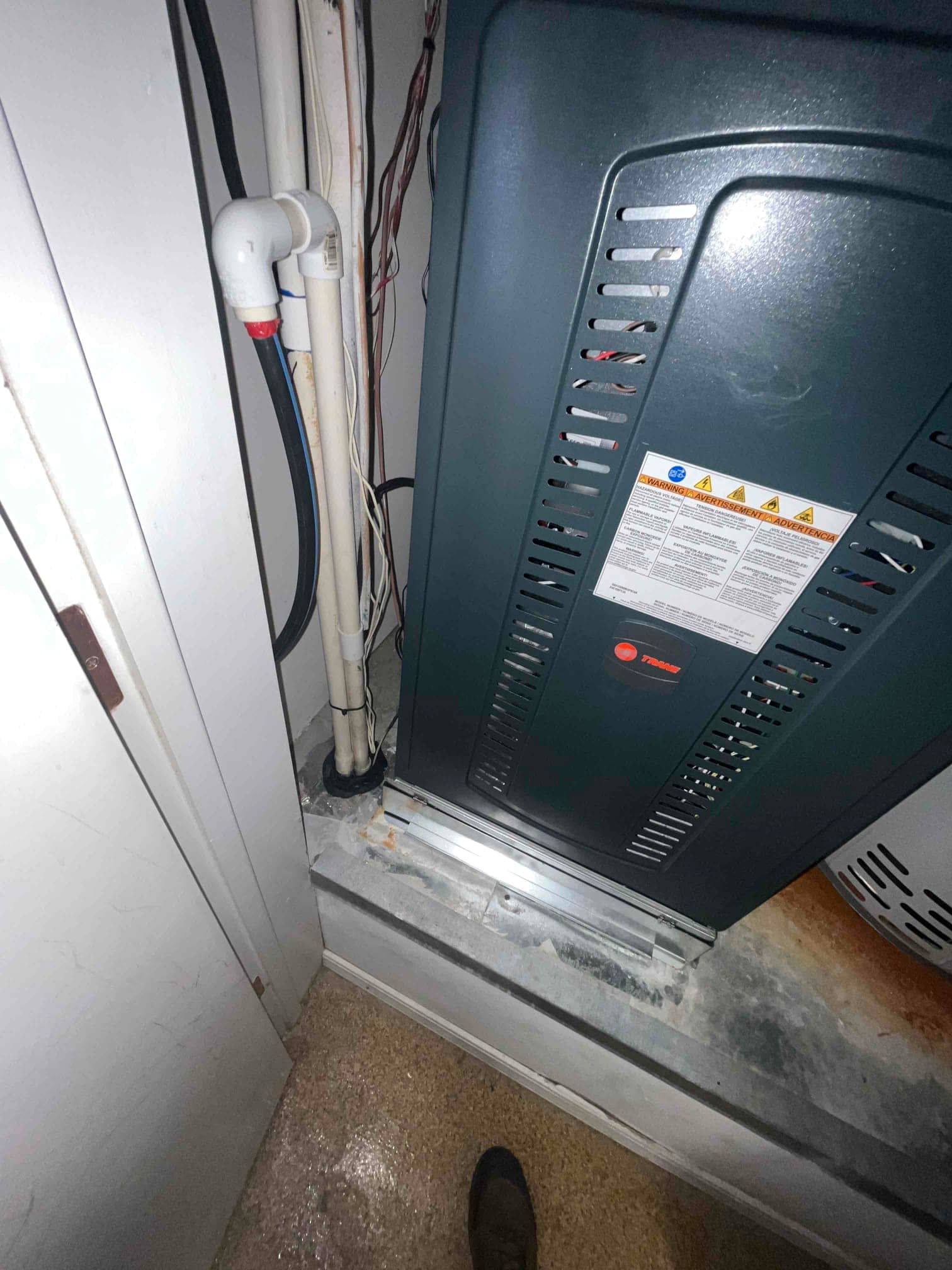 New gas furnace set on a platform with connected PVC condensate drain and routed control wiring in a utility closet.