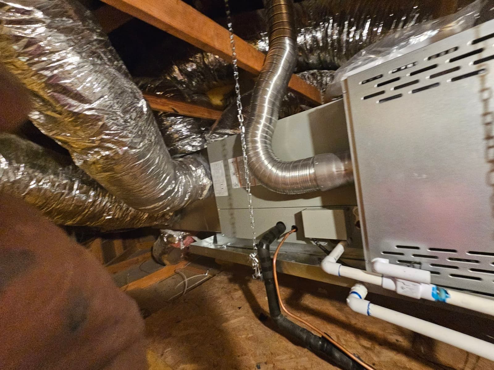 New horizontal air handler suspended in attic with insulated duct connections, condensate drain piping, and refrigerant line set routed and insulated.