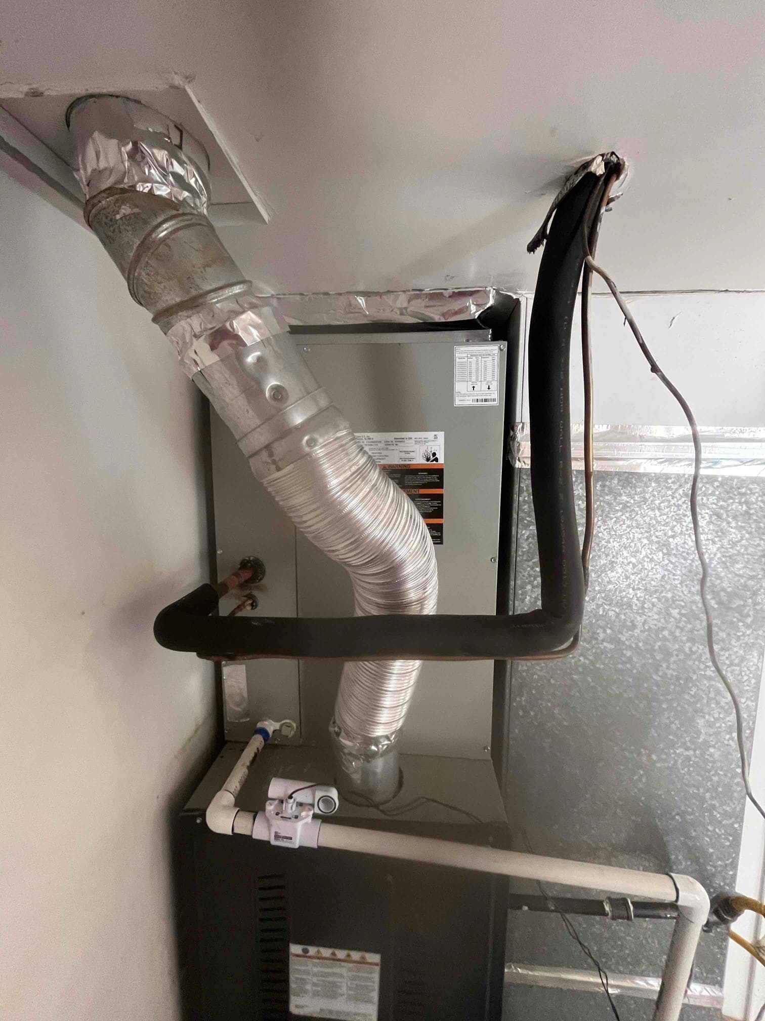New indoor furnace and evaporator installed with insulated refrigerant lines, sealed flue venting, and condensate drain with inline safety switch.