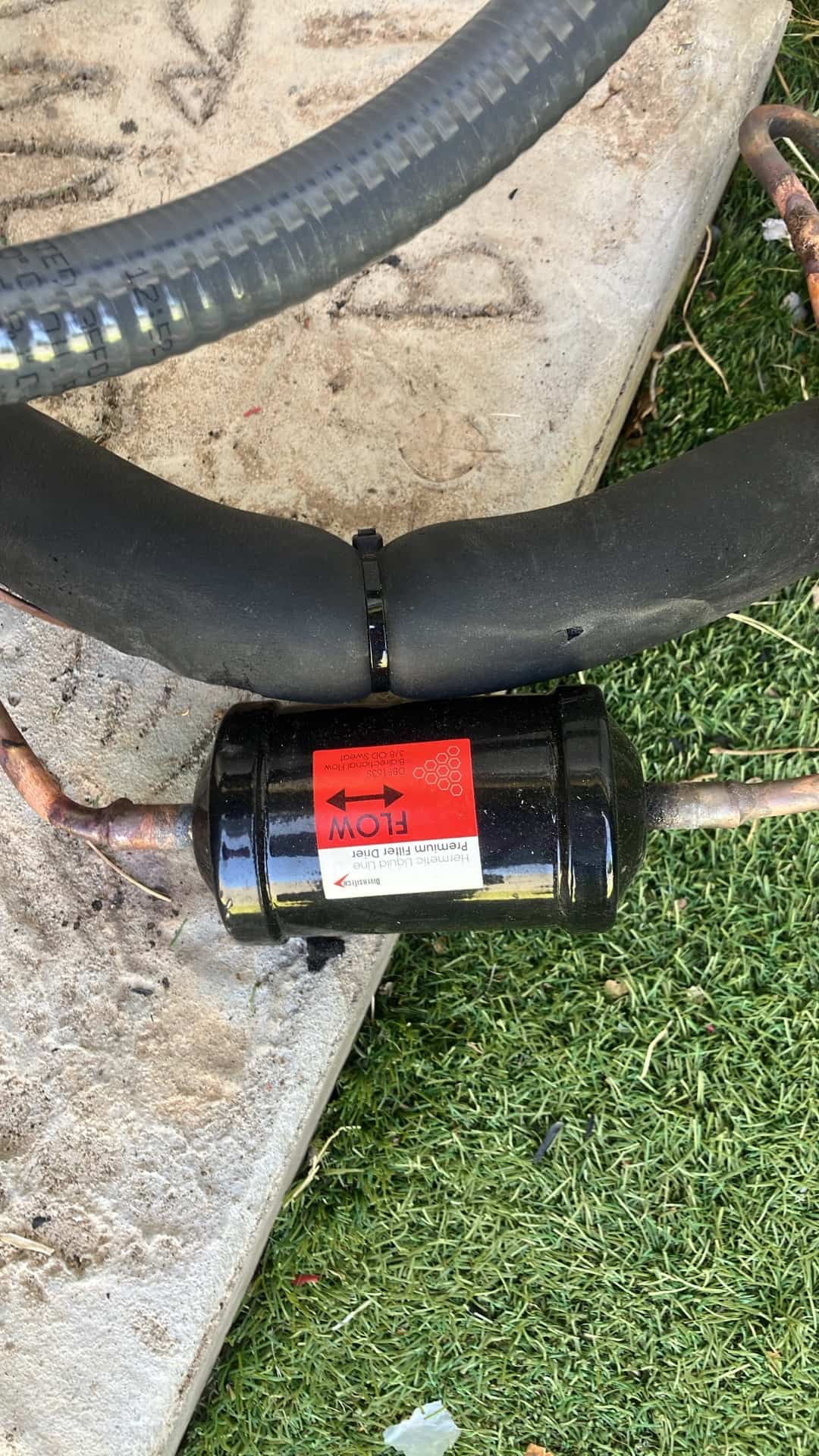 New liquid-line filter drier installed with flow direction indicated, alongside insulated suction line at the outdoor unit.