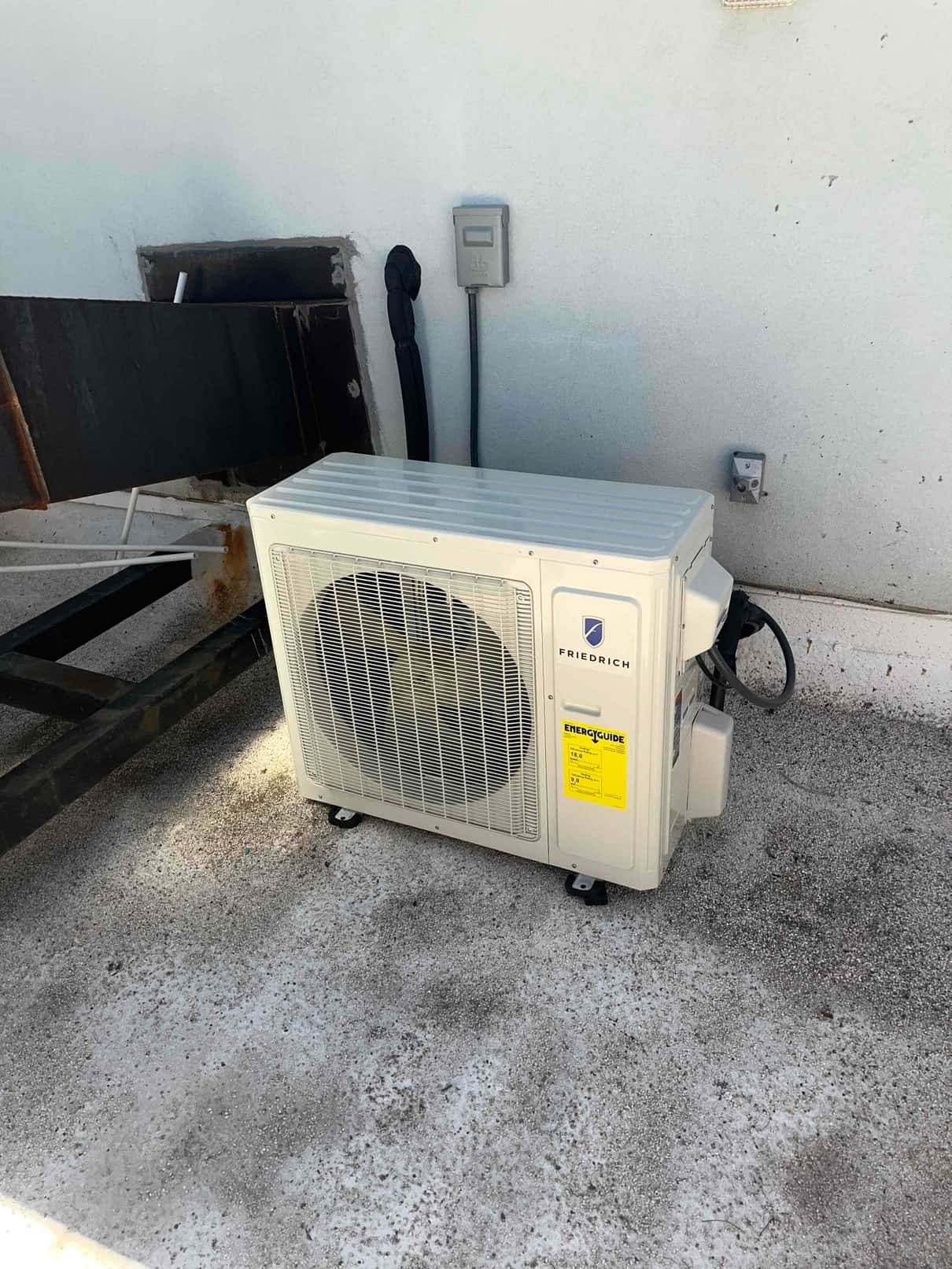 New mini-split outdoor condenser set on a level surface with insulated line set and exterior disconnect installed.