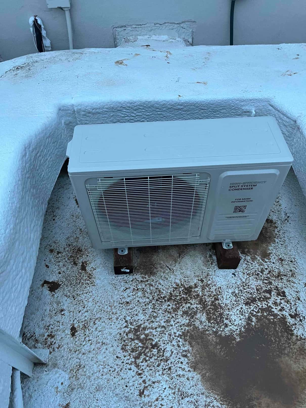 New mini-split outdoor condenser set on riser blocks on a coated rooftop with sealed wall penetration and electrical whip.