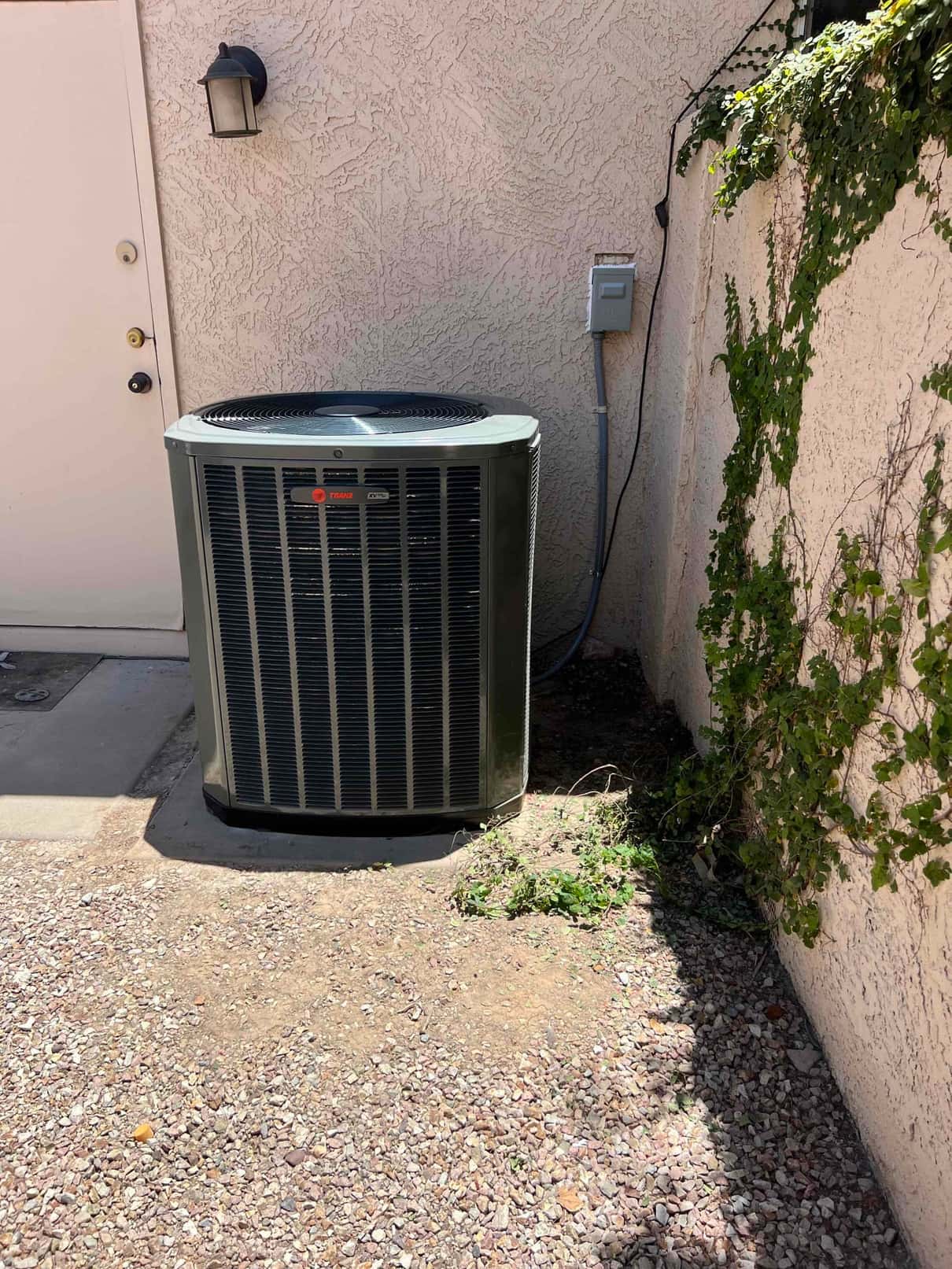 New outdoor condenser set beside the home with electrical disconnect mounted and line set routed along the wall.