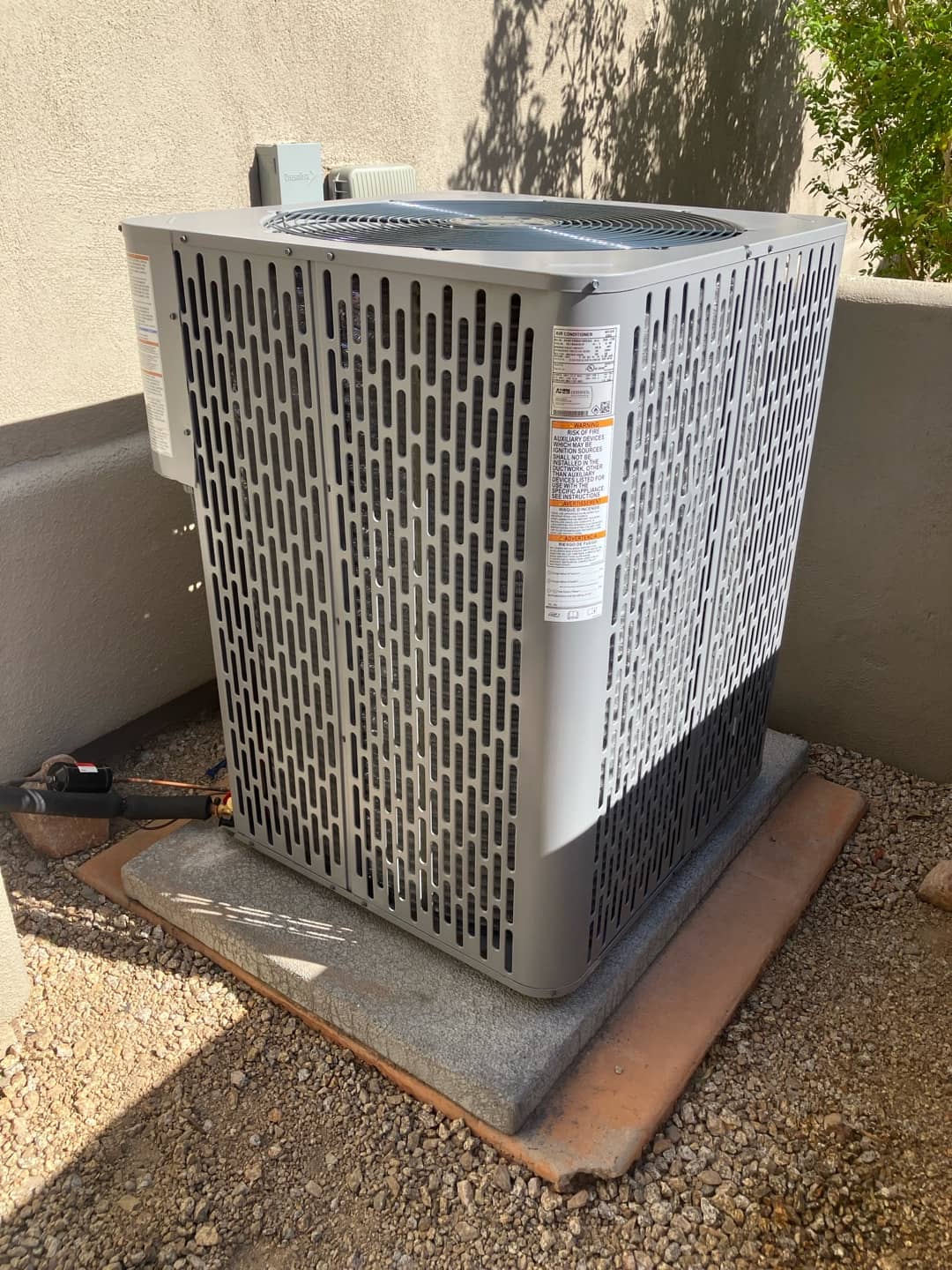 New outdoor condenser set on a level pad with insulated line set and wall-mounted disconnect in place.