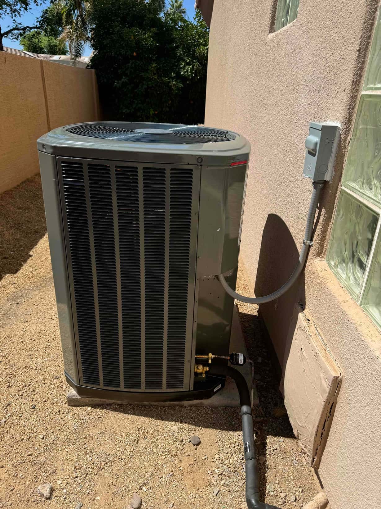 New outdoor condenser set on a level pad with insulated refrigerant line, electrical whip, and weatherproof disconnect mounted nearby.