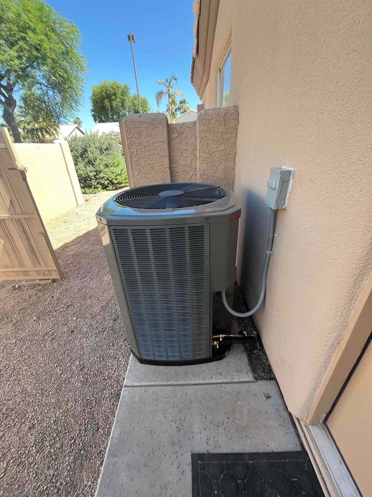 New outdoor condenser set on a level pad with sealed line set penetration and mounted electrical disconnect beside the unit.