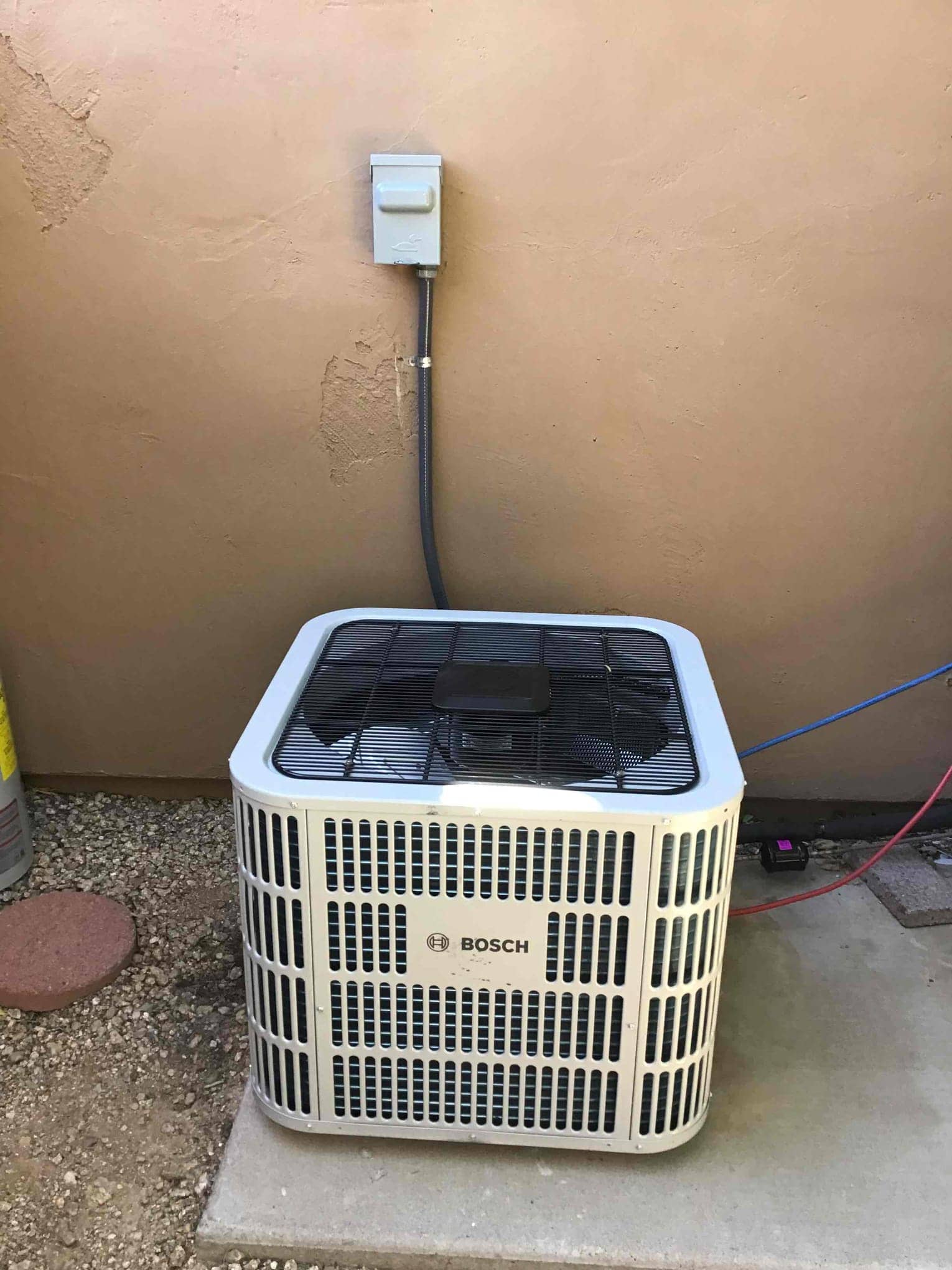 New outdoor condenser set on a level pad with weatherproof disconnect mounted and liquid-tight conduit connection to the unit.
