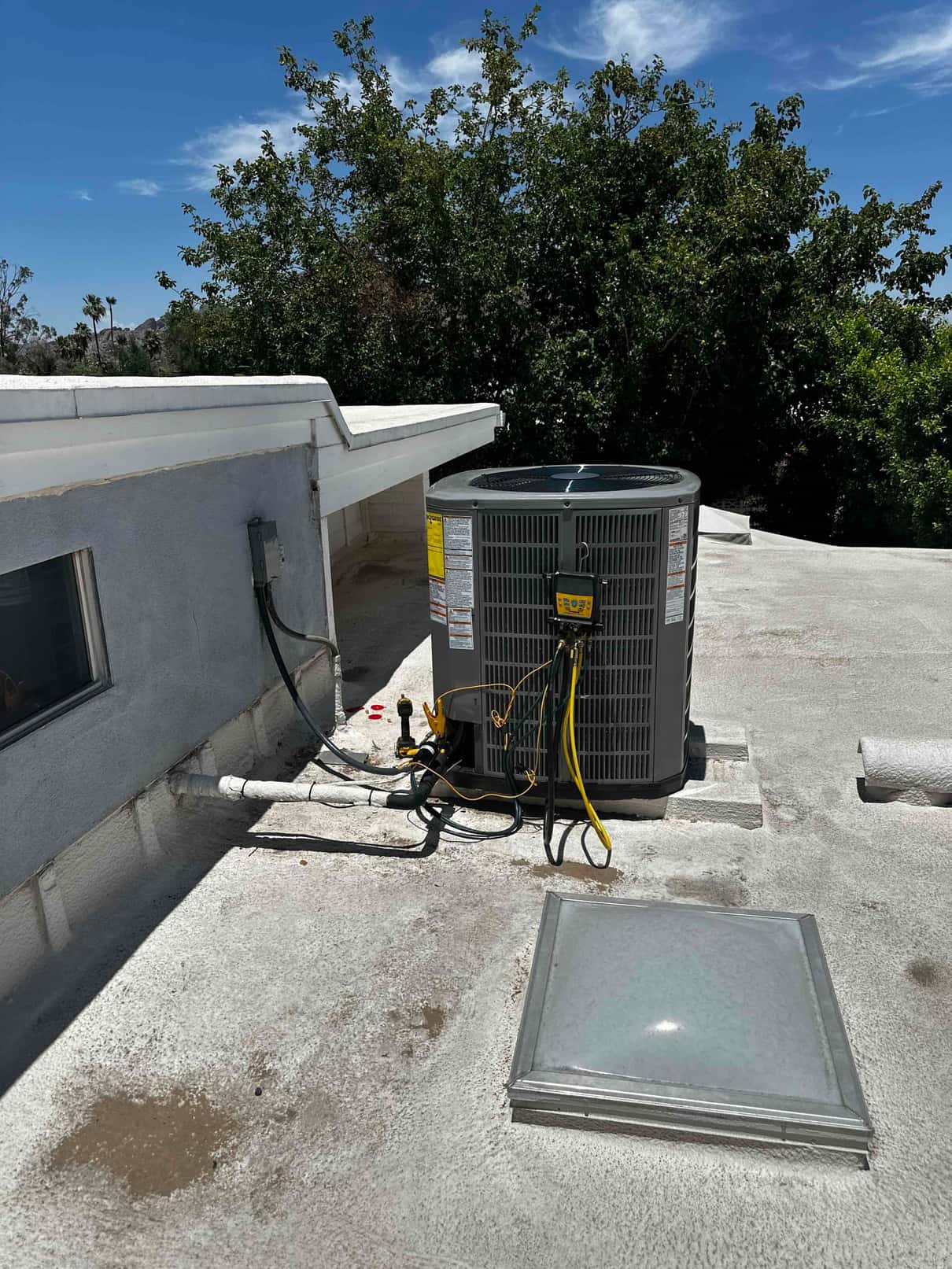 New outdoor condenser set on rooftop blocks with insulated line set, electrical disconnect, and service gauges connected during installation.