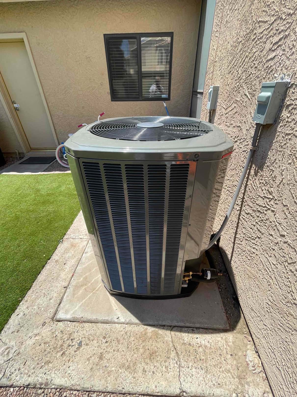 New outdoor heat pump condenser installed on a level pad with insulated line set and weatherproof disconnects mounted on the wall.