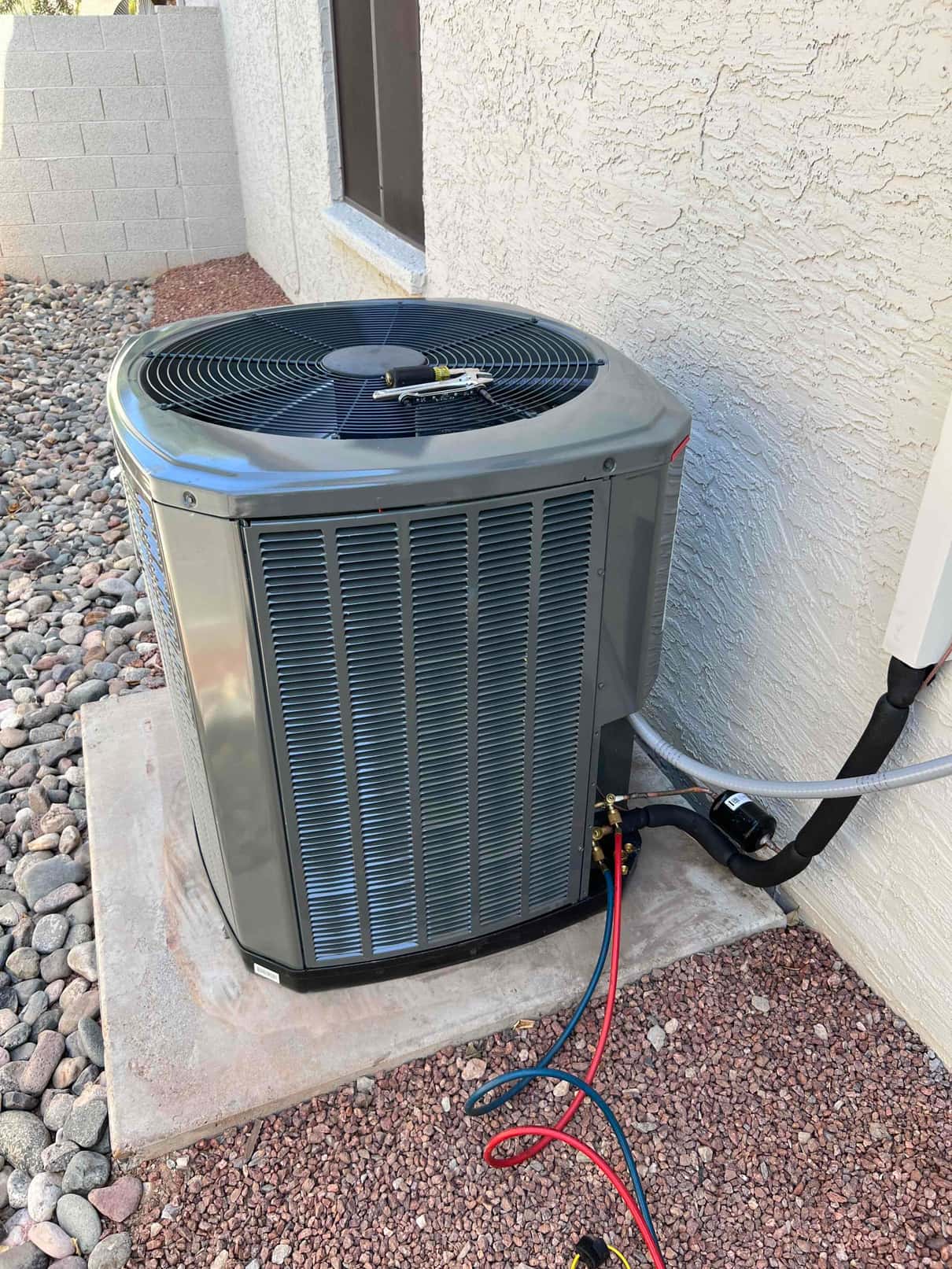New outdoor heat pump condenser set on a level pad with insulated line set and service hoses connected at the valves.