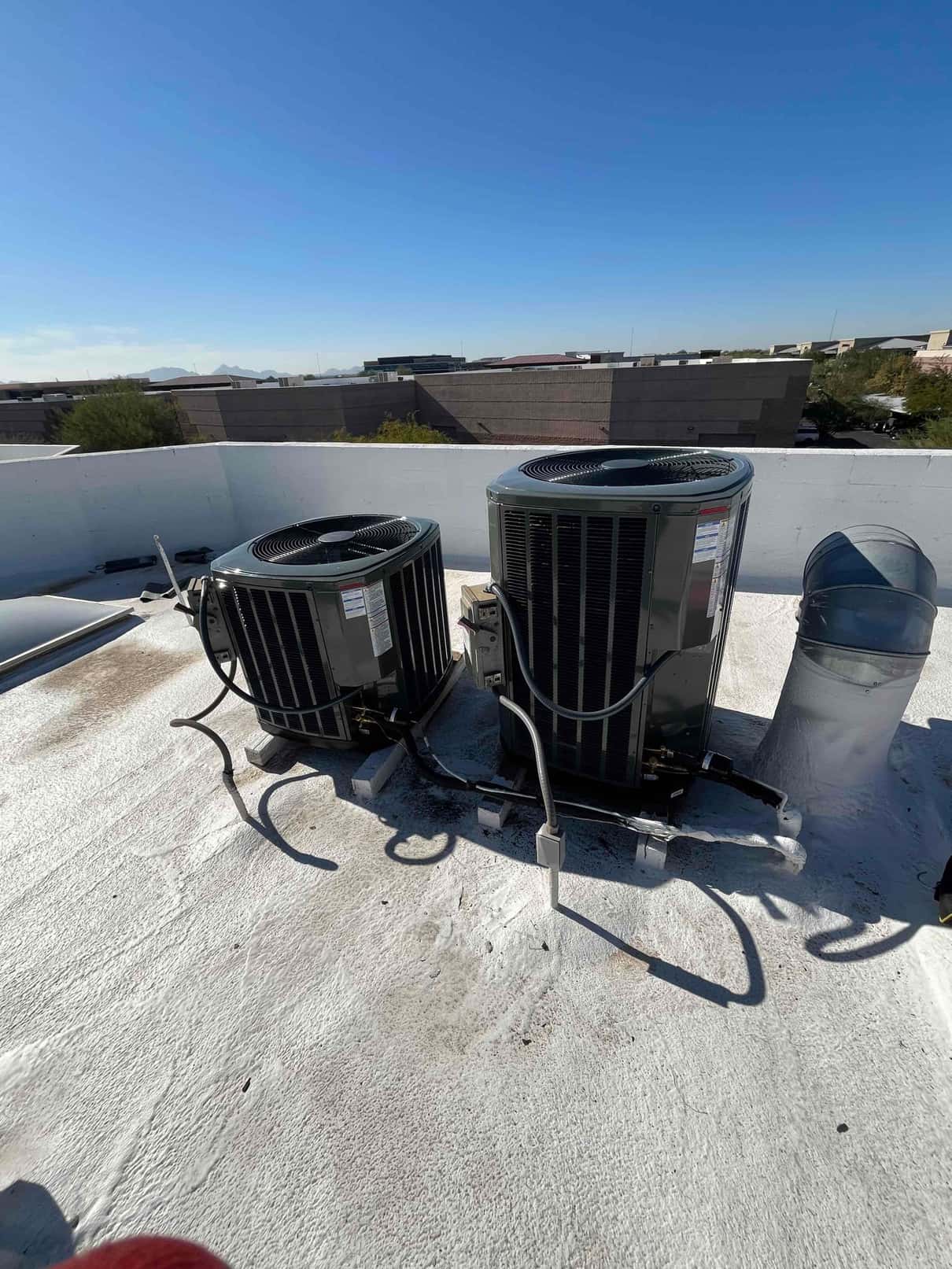 Two new outdoor heat pump condensers set on rooftop supports with secured electrical whips and insulated line sets.