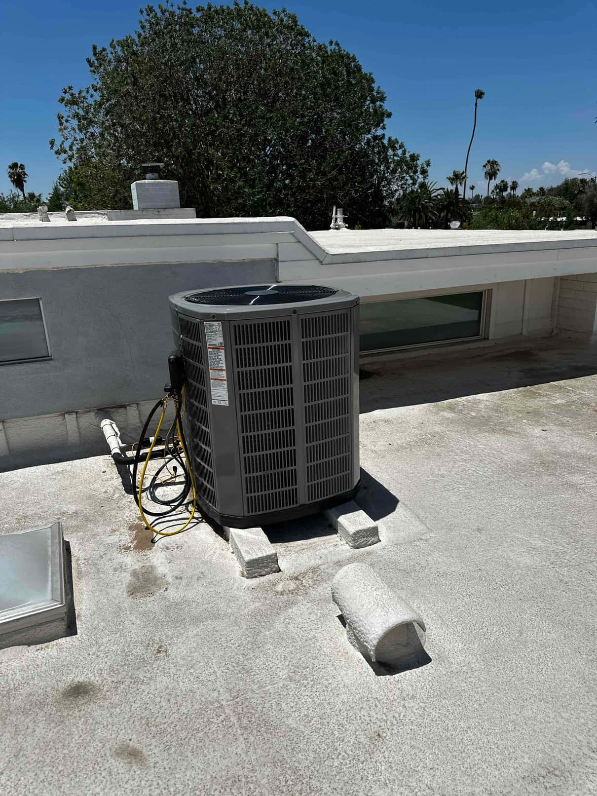 New rooftop condenser set on riser blocks with connected refrigerant lines and condensate drain, showing a clean installation site.