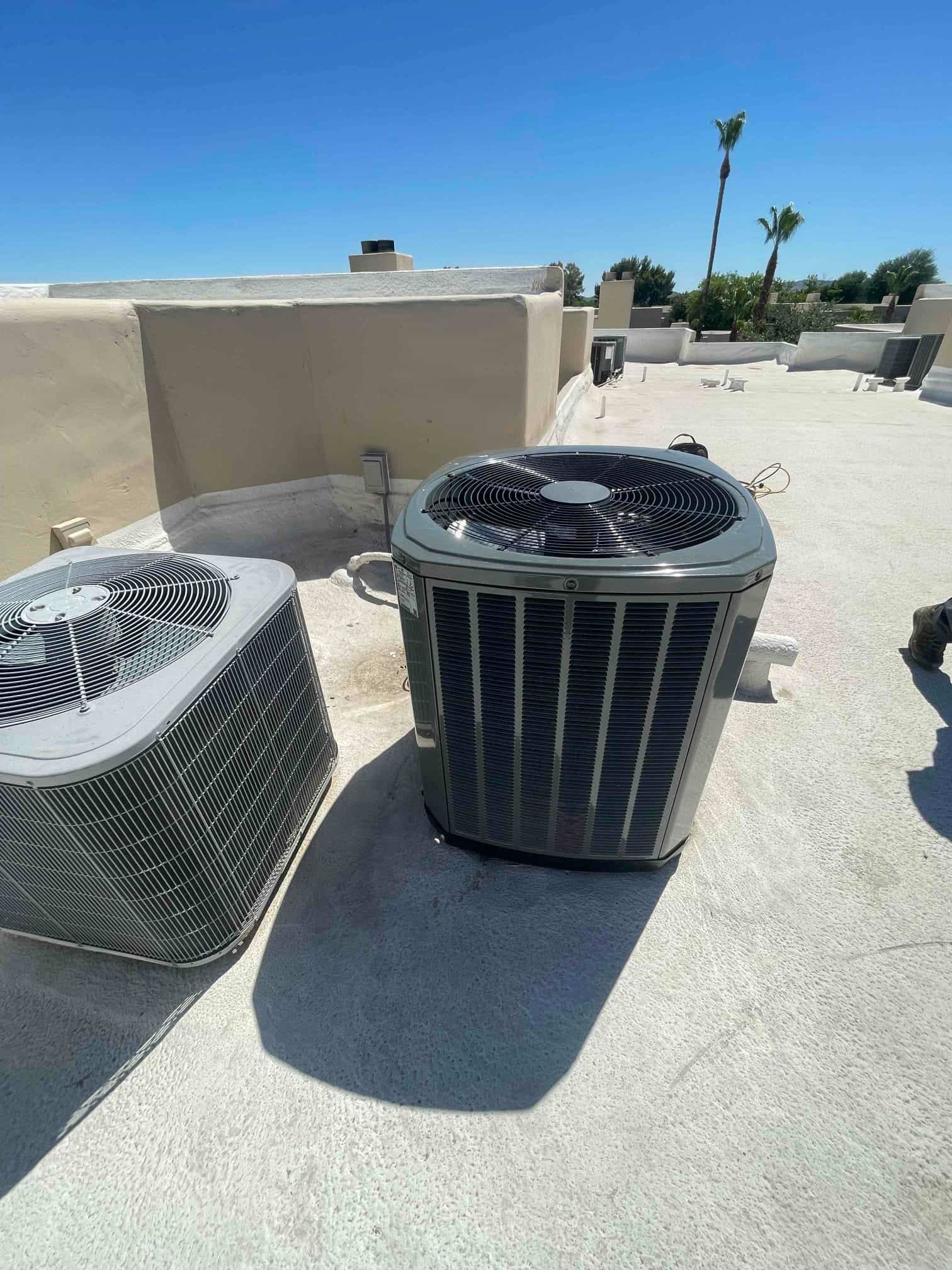 New rooftop heat pump condenser set on a level surface beside an older unit, with electrical disconnect and line set nearby.
