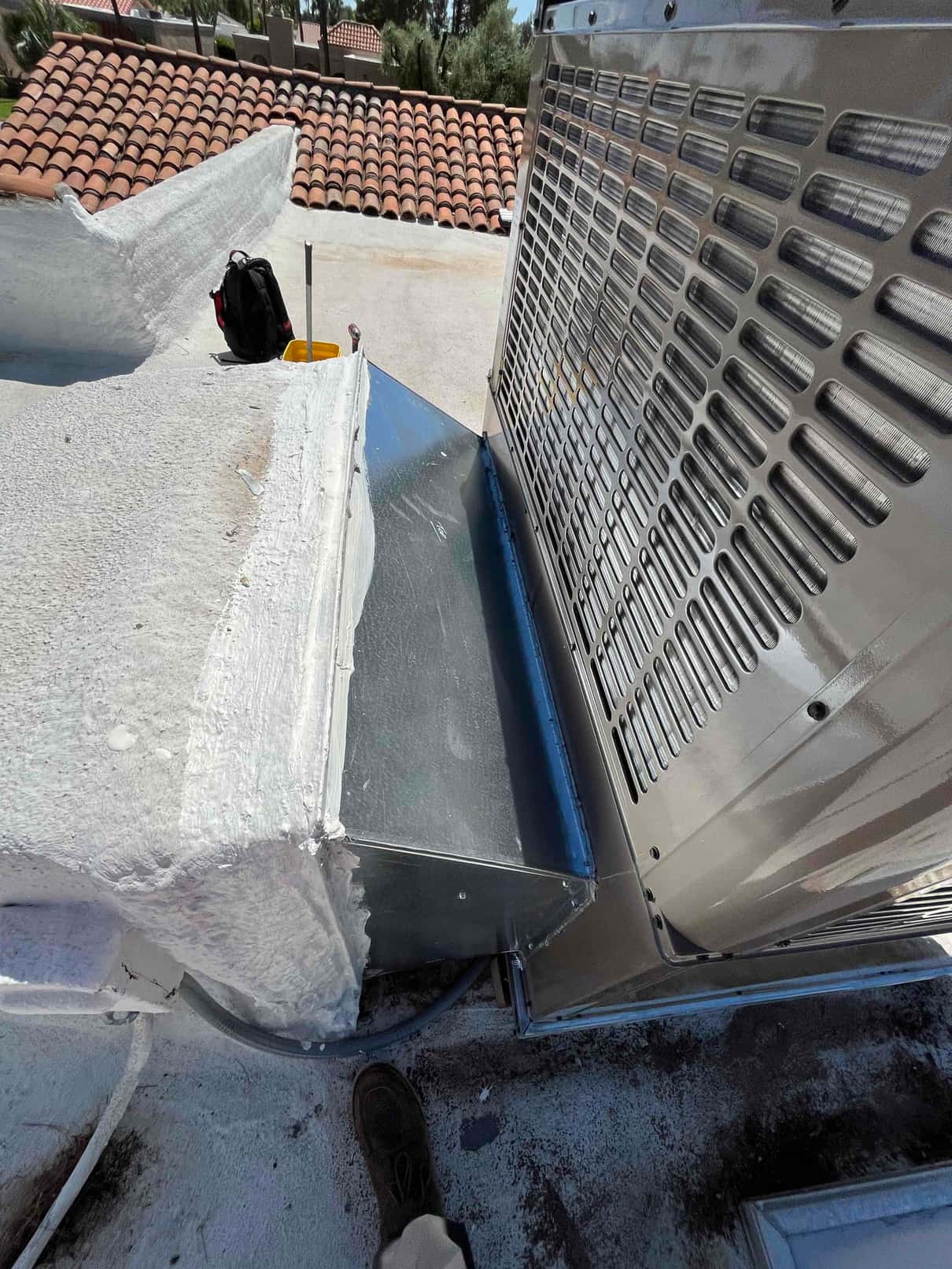New rooftop package unit connected to a sealed sheet-metal curb adapter with mastic applied at the roof transition.