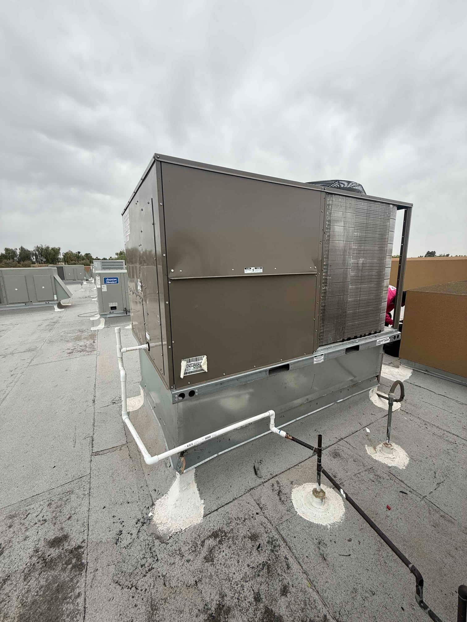 New rooftop package unit set on a curb with connected condensate drain and gas piping, secured and sealed to the roof.