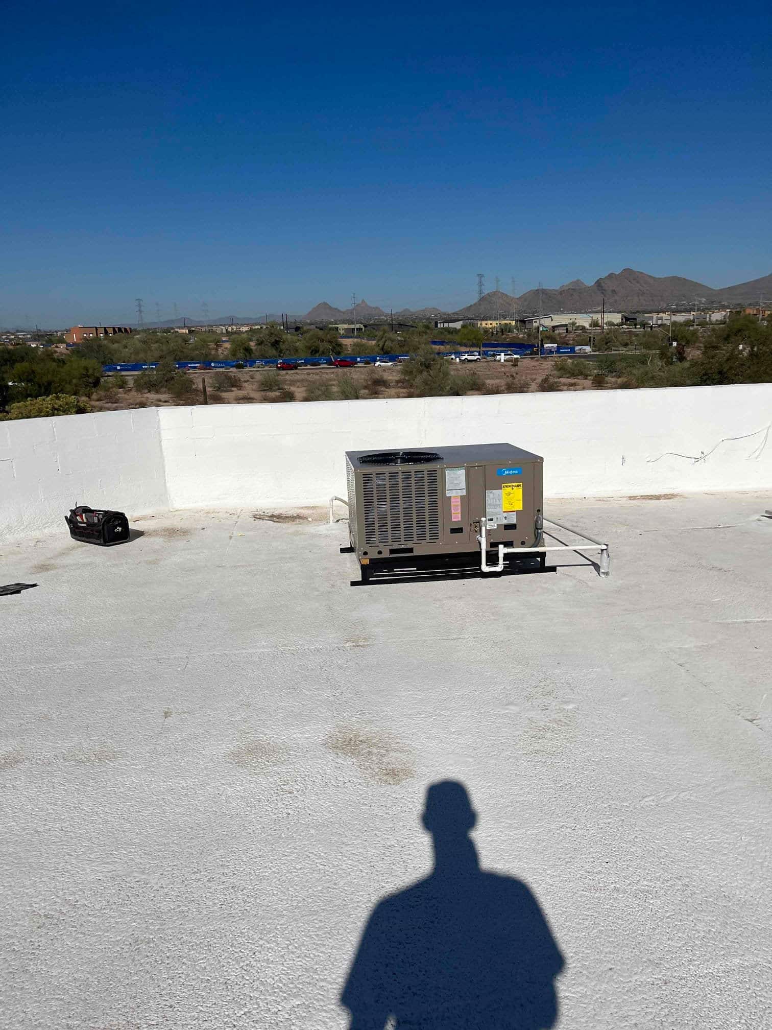 New rooftop packaged HVAC unit installed on a flat roof with insulated condensate drain and support stand visible.