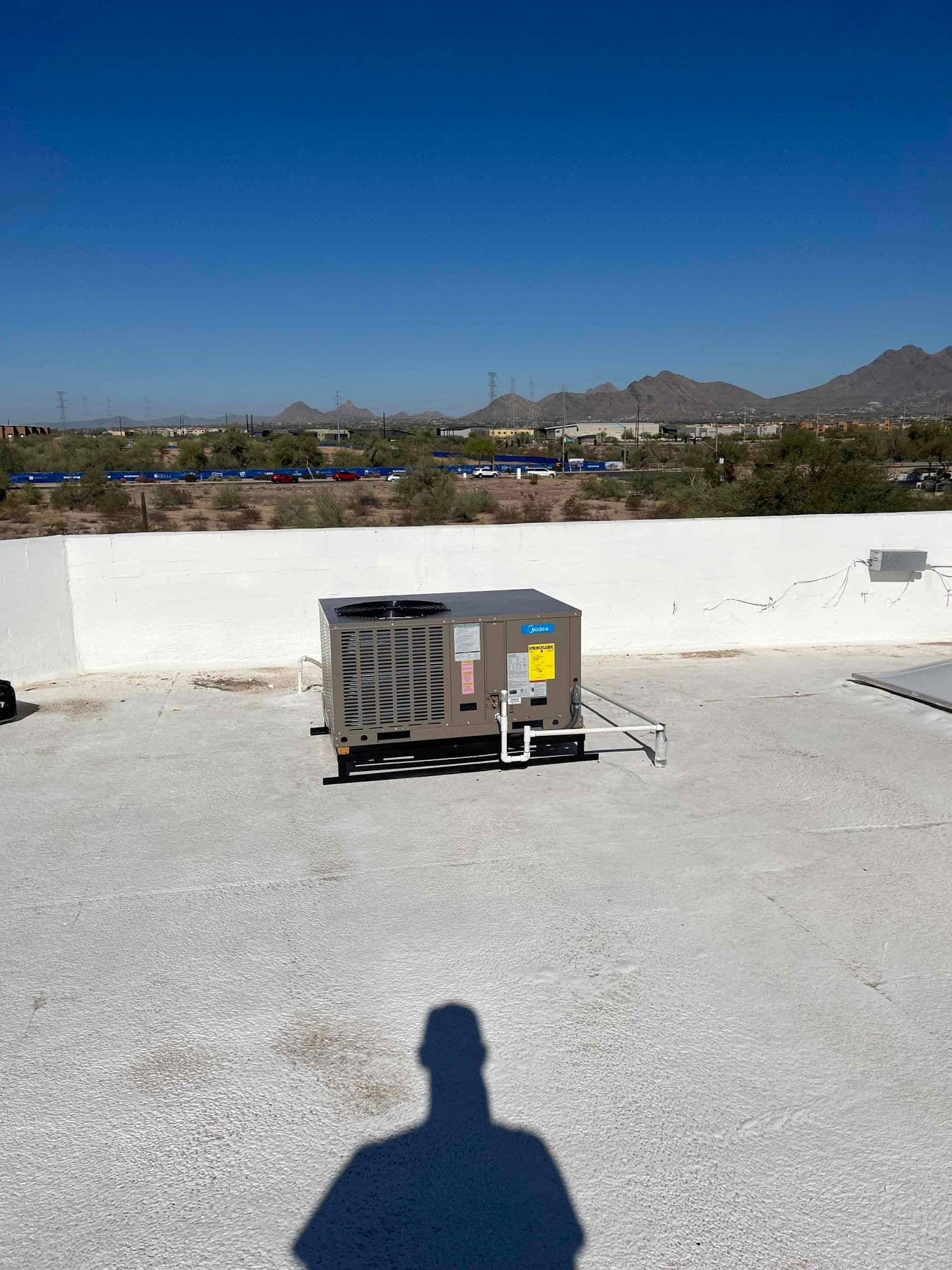 New rooftop packaged HVAC unit set on a level surface with connected condensate drain and protected refrigerant/utility lines.