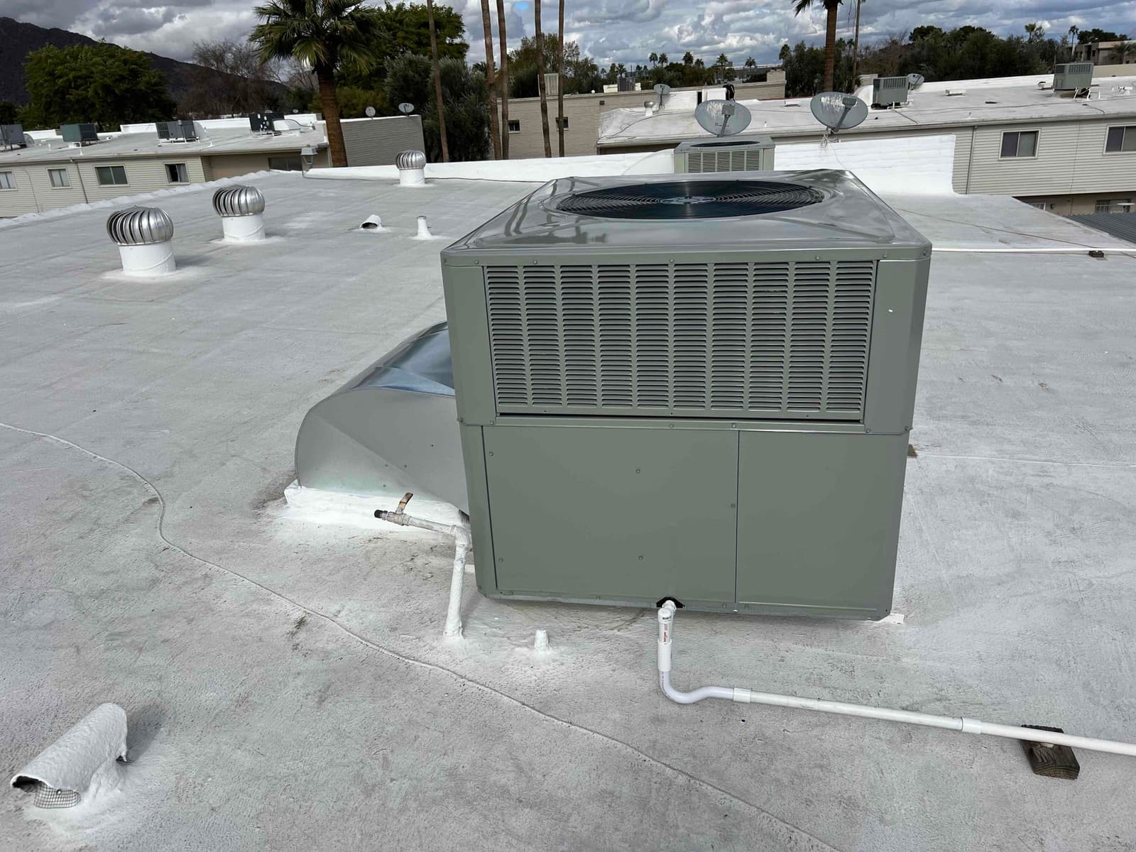 New rooftop packaged HVAC unit set on a sealed roof curb with condensate drain piping routed across the roof surface.