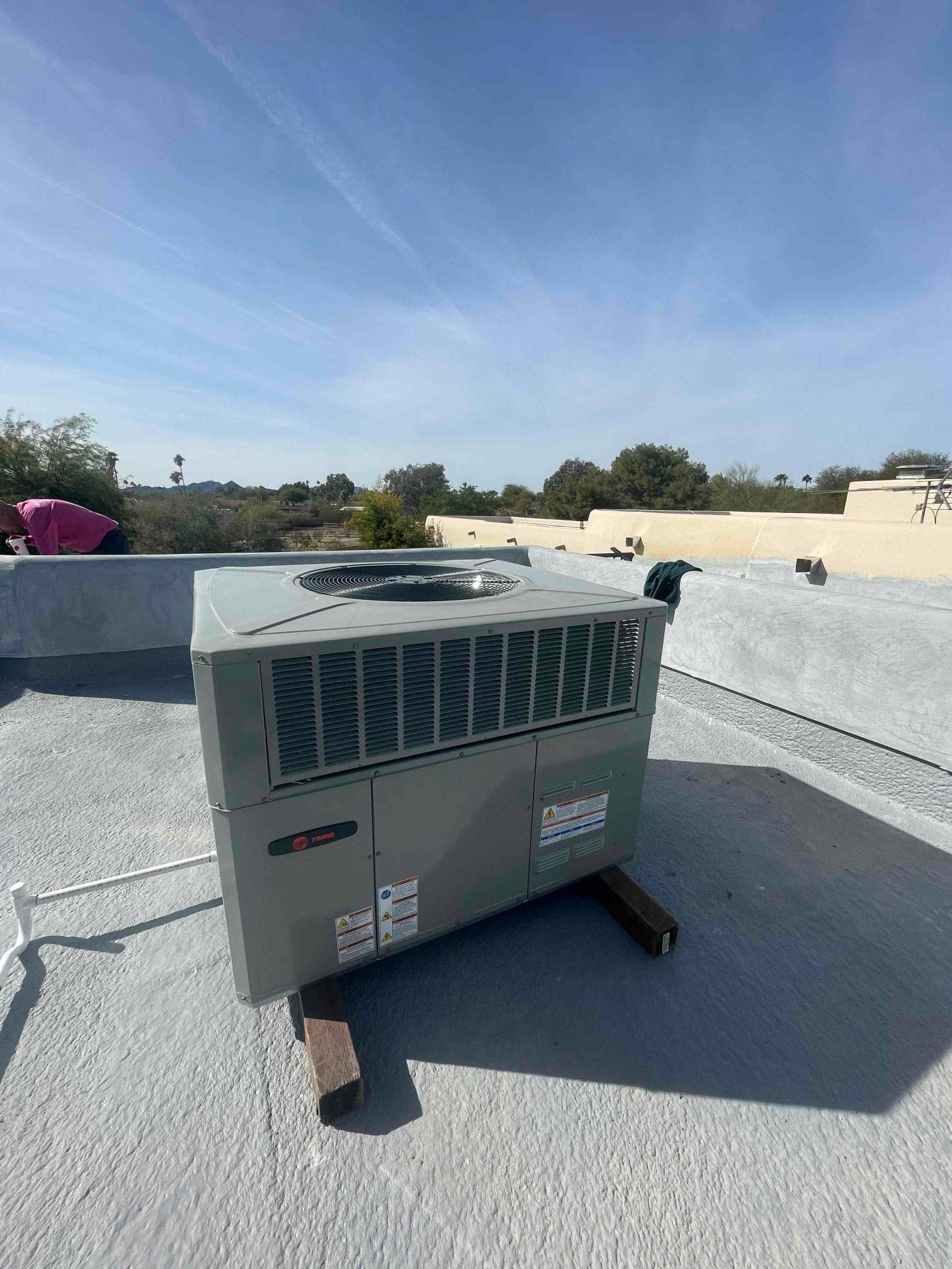 New rooftop packaged HVAC unit set on wood risers with electrical and drain connections routed along the roof surface.