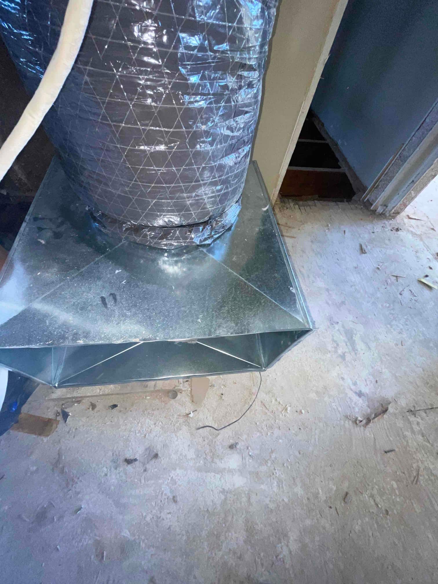 Newly installed metal supply plenum transitions to insulated flex duct, set in place on a construction floor during installation.